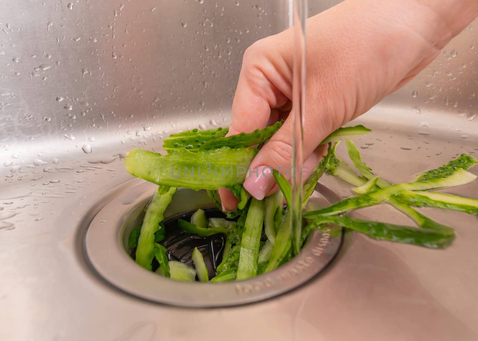 Disposing of cucumber peels in a stainless steel sink with a garbage disposal.