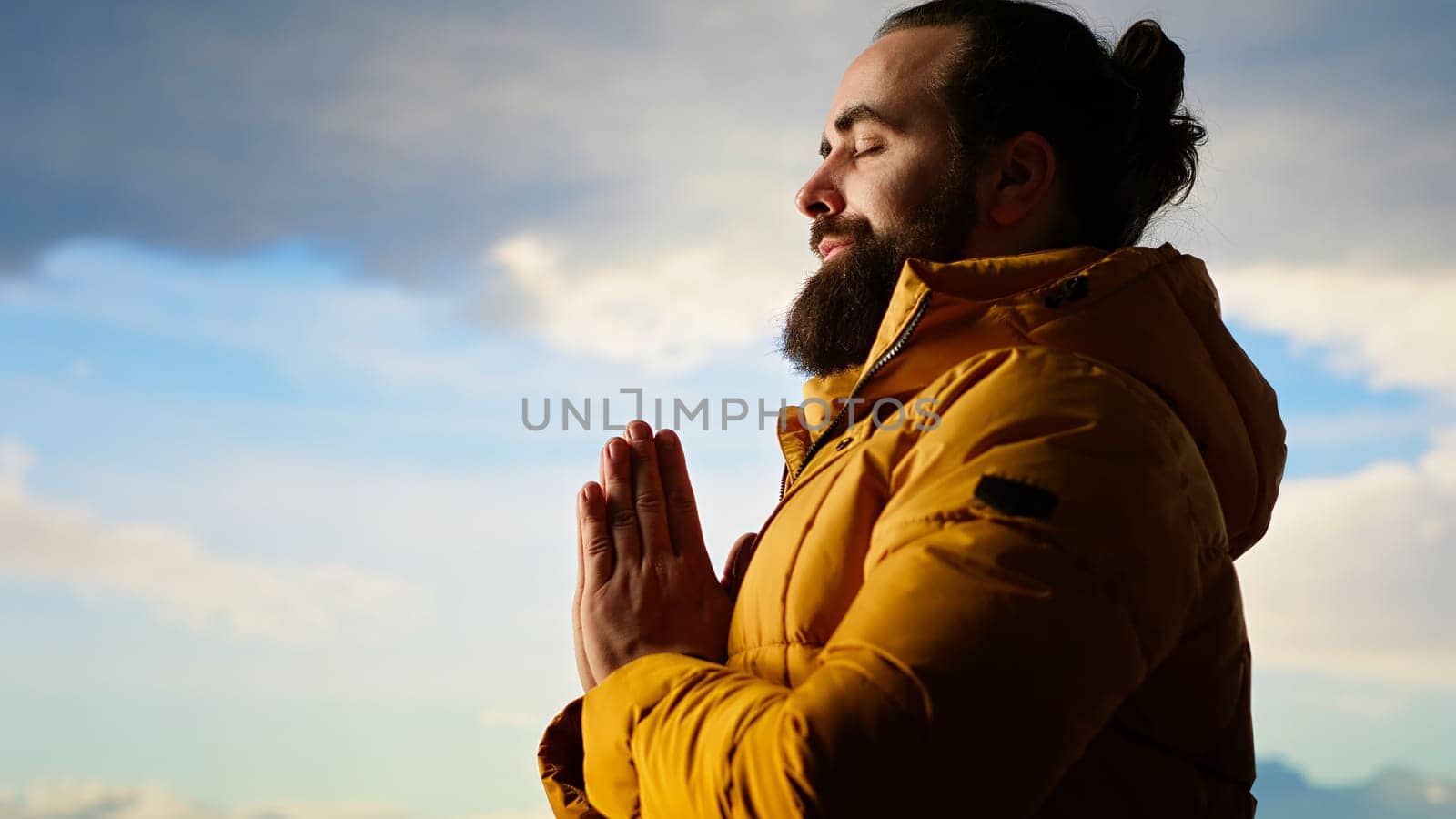 Adventure seeker doing a meditation pose on top of the mountain, successfully climbing the hill and enjoying the scenic landscape. Young calm zen traveler hiking and meditating. Camera B.
