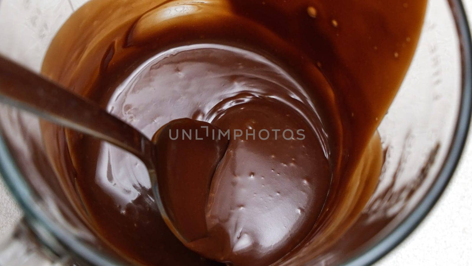 Close-up of a chocolate fudge in a glass measuring cup with a spoon.
