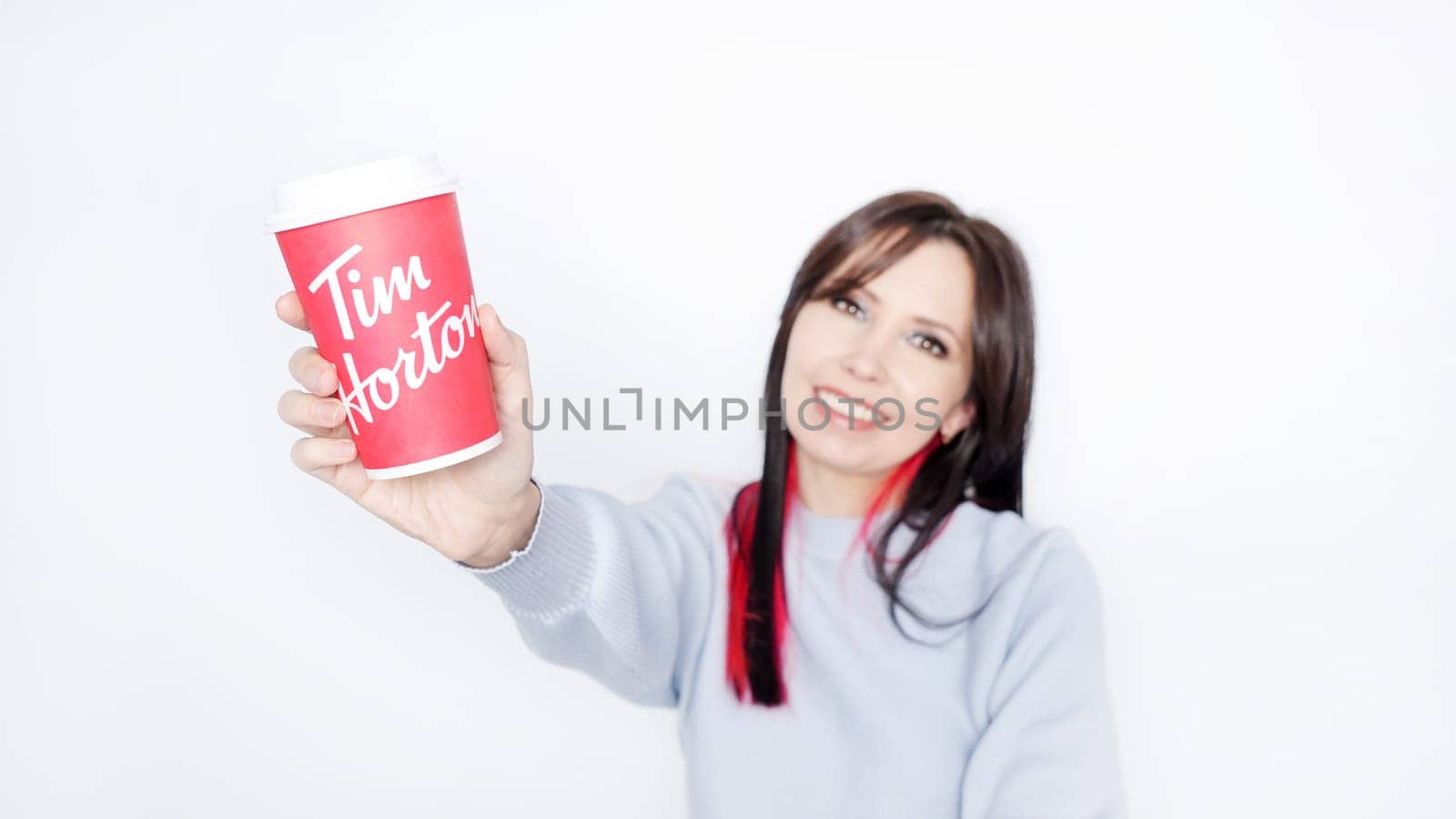 Cheerful Young Woman with Long Dark Hair Enjoying Tim Hortons Warm Cup of Coffee in Cozy Blue Sweater - Ottawa ON Canada -2024-10-28