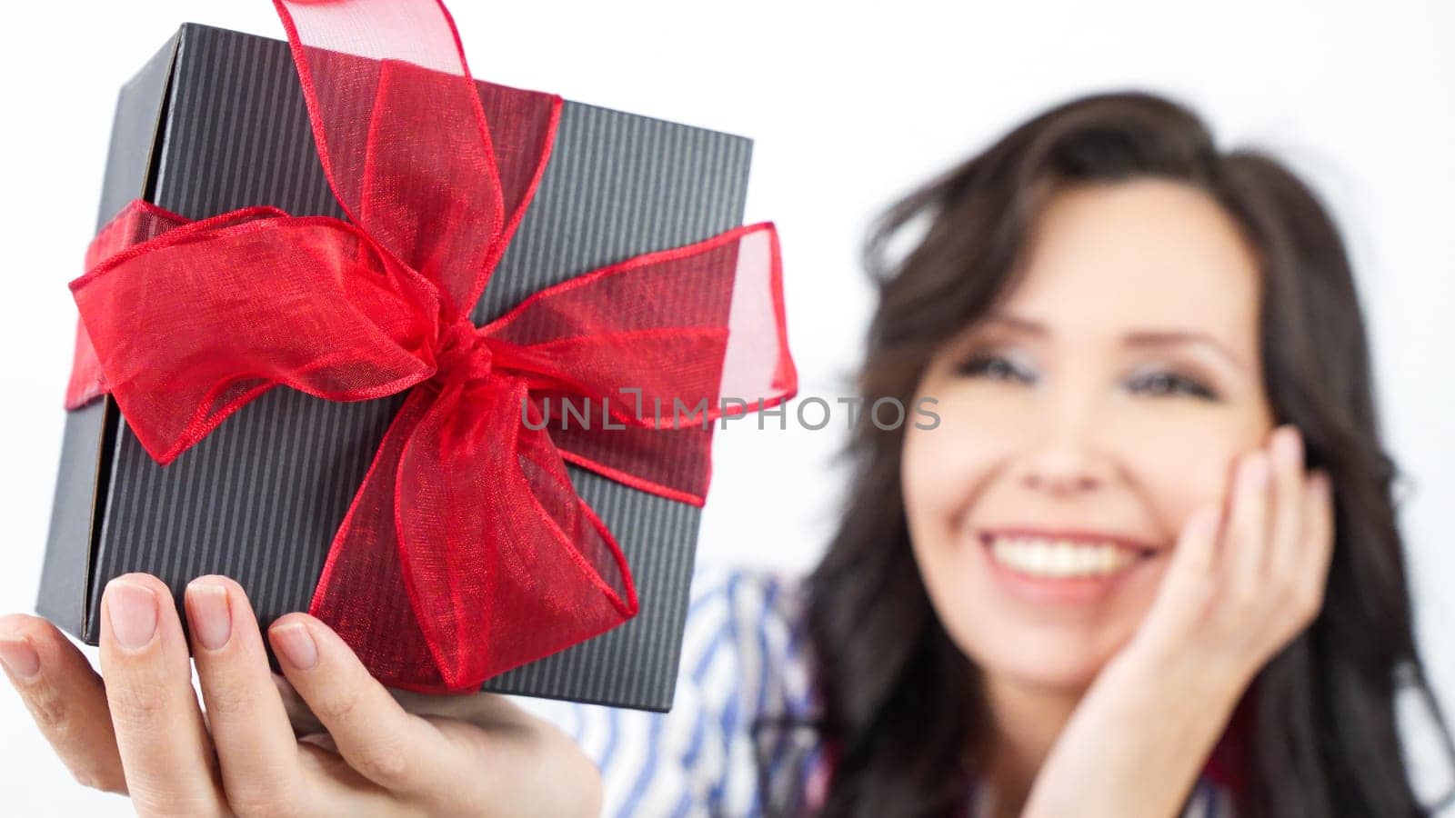 A cheerful woman looks at the camera with a warm smile, wearing a trendy casual outfit. Her long, dark hair enhances the soft, neutral background, creating a joyful and inviting atmosphere.
