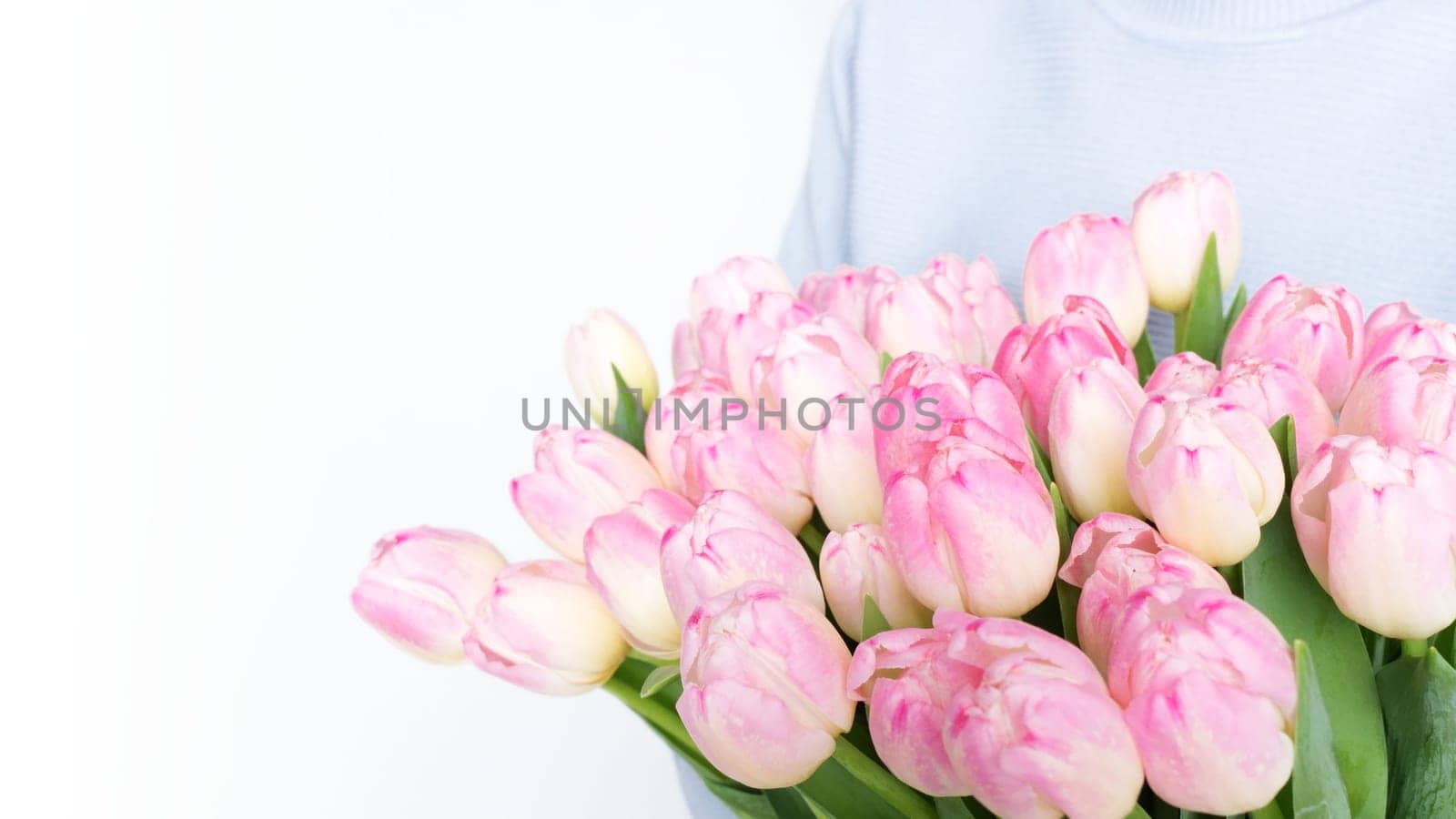 Woman holding a beautiful bouquet of vibrant pink tulips with green foliage against a white background. The pink tulips are striking and complement the womans attire perfectly.