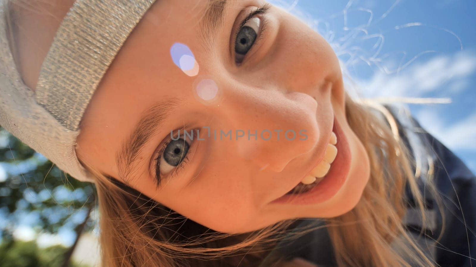 Portrait of a cheerful school girl wearing a white baseball cap, smiling broadly and showing her blue eyes on a bright sunny day