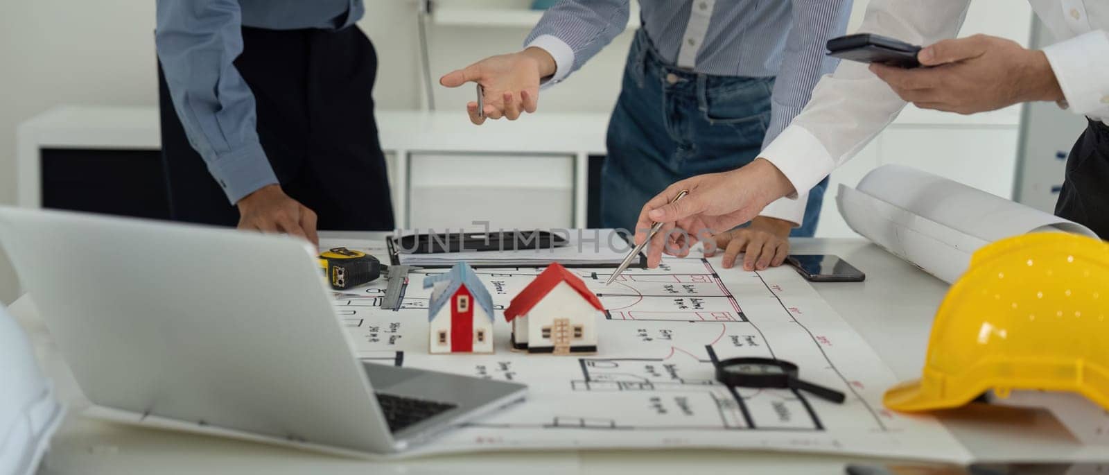 A team of professionals collaborates on construction blueprints, employing tools and models to visualize their project. They engage actively in discussions to enhance planning accuracy.