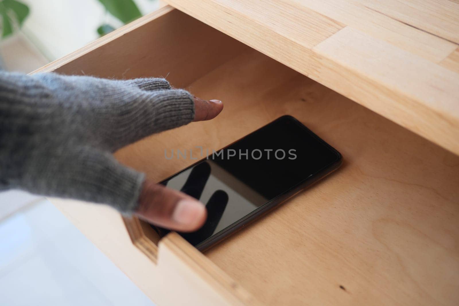 Hand with gloves stealing a for smartphone in wooden drawer .