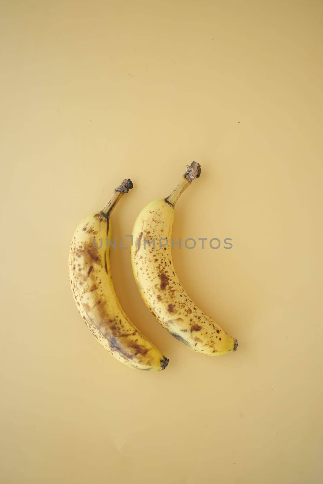 Two ripe bananas with brown spots arranged on a plain light backdrop.