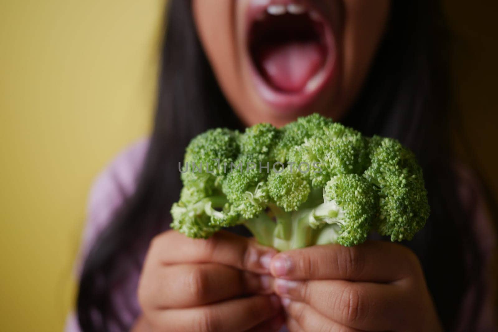 A child joyfully shows off a bunch of broccoli with a big smile.