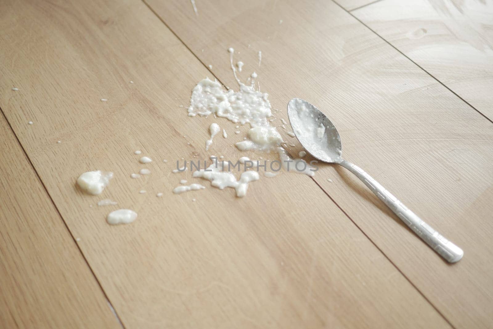 Spilled yogurt on wooden floor with spoon ,