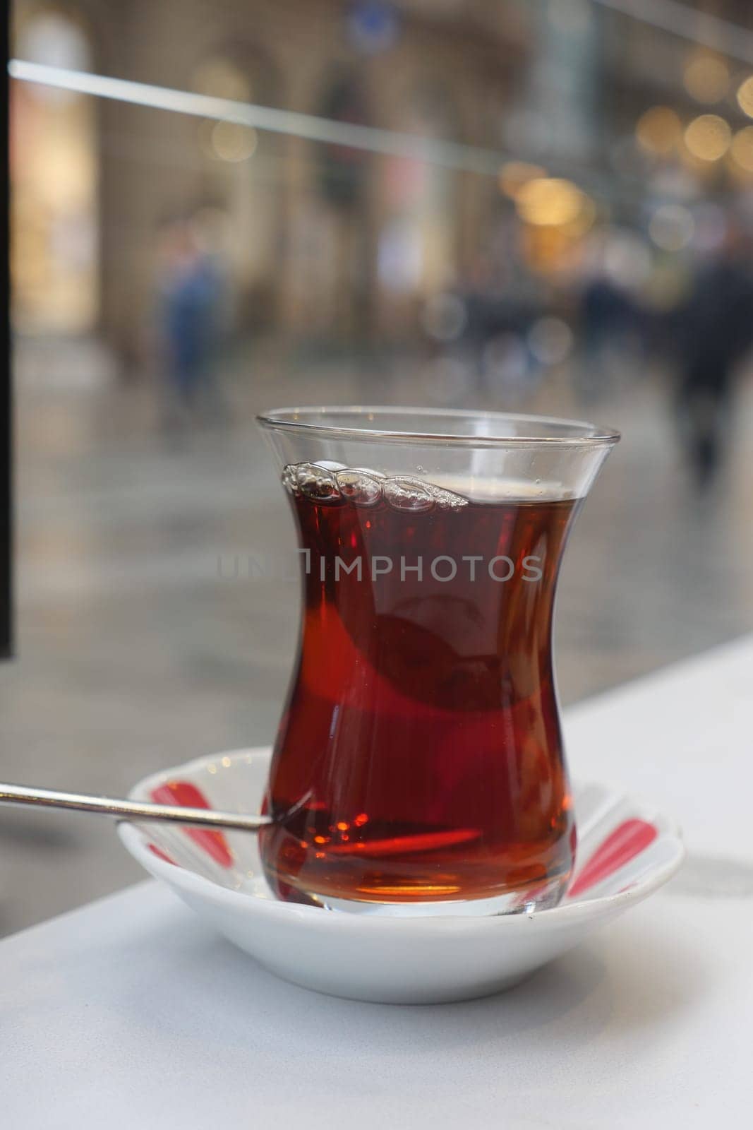 Hot Turkish tea in a delicate glass cup sits on a plate in a bustling area.