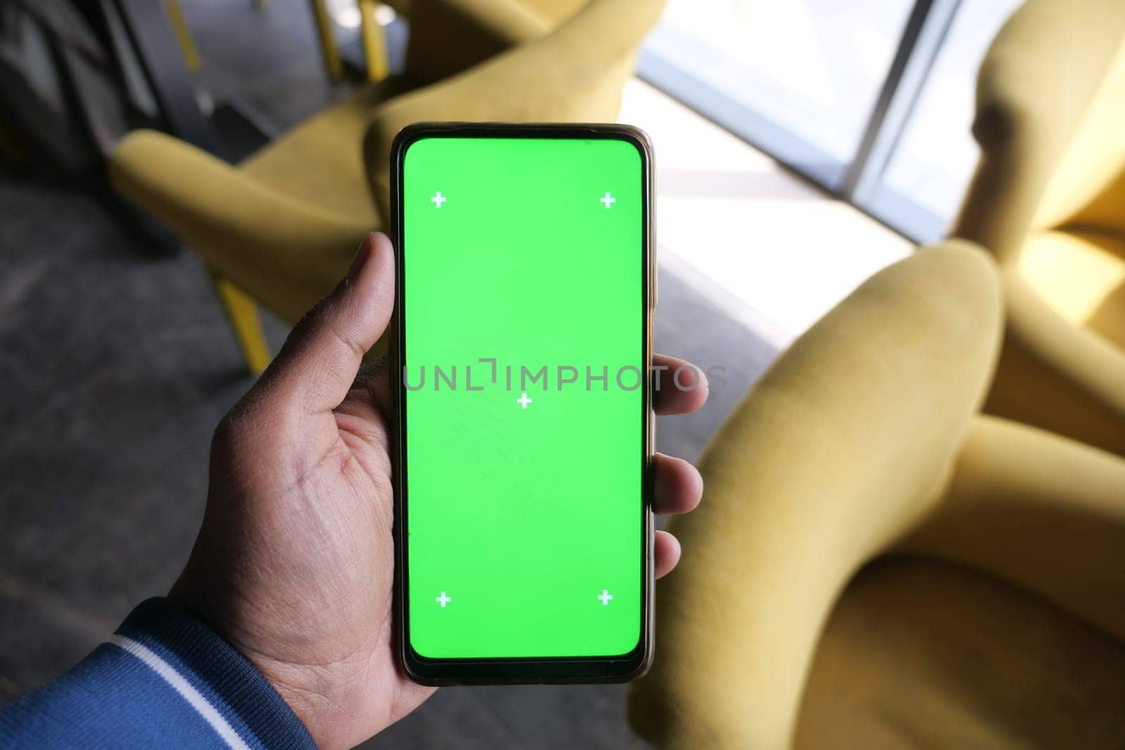 A hand holds a smartphone showing a bright green screen indoors.
