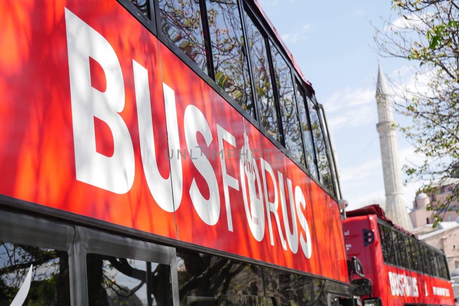 Bright red tour bus parked on urban street with historic mosque nearby.