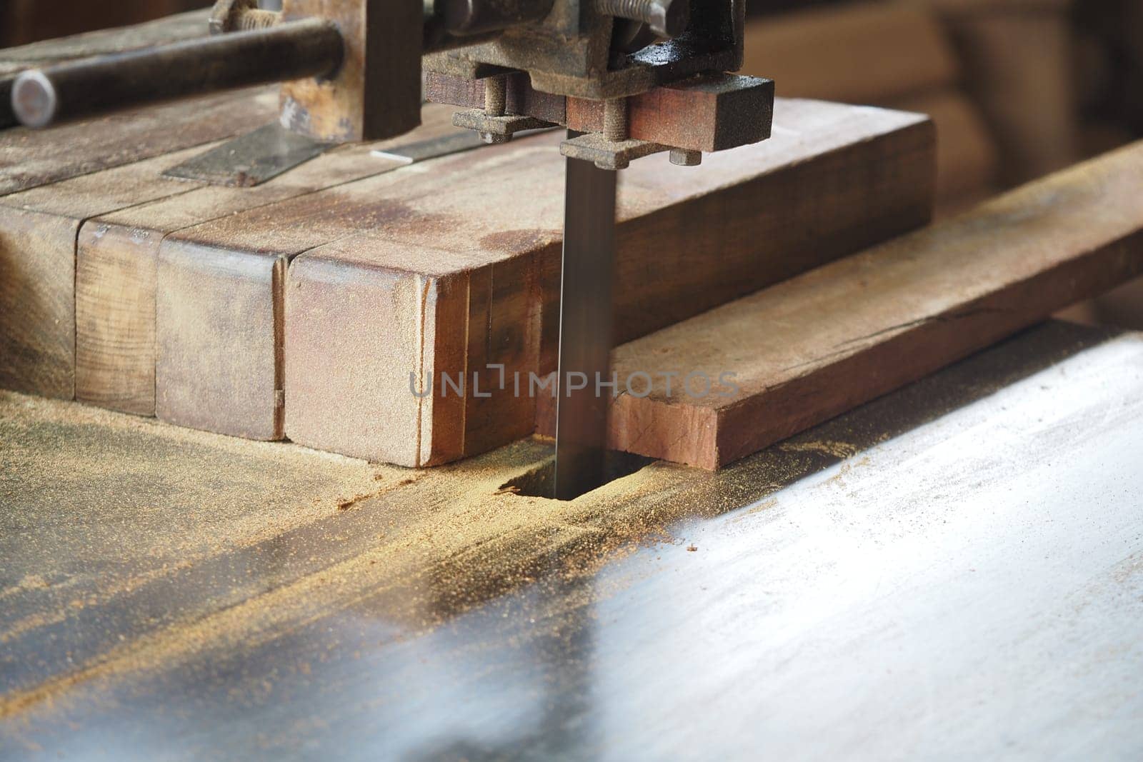A bandsaw is cutting through a wooden plank in a workshop.
