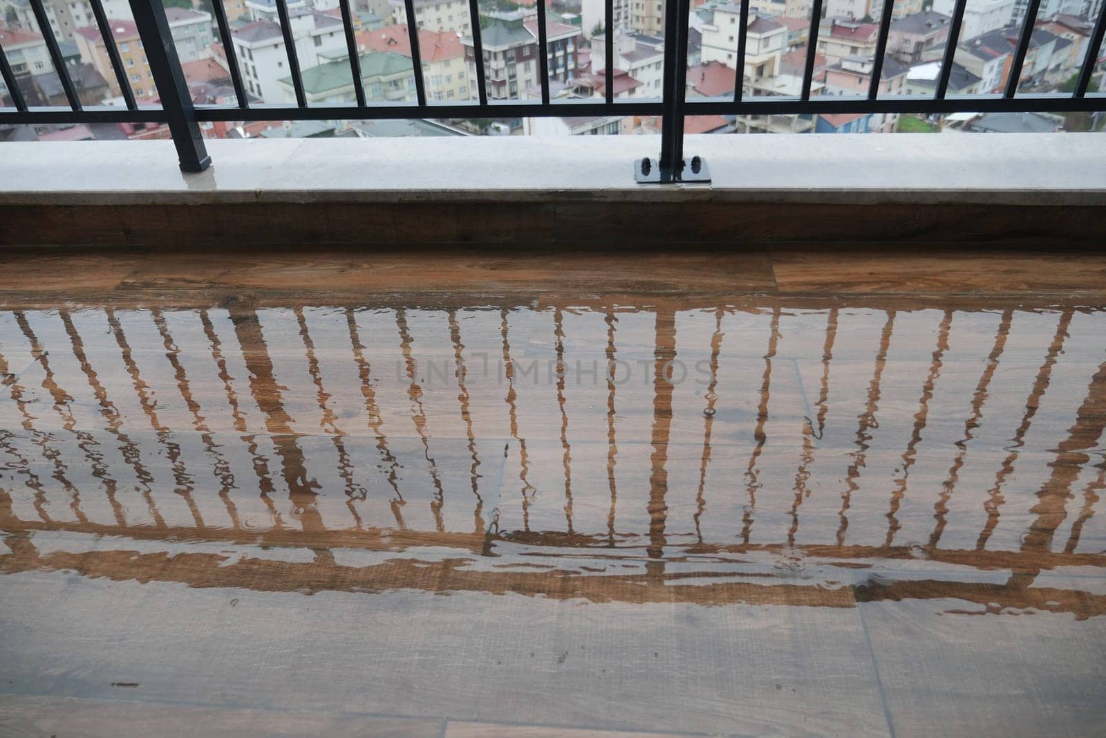 Raindrops create puddles on the balcony floor reflecting buildings.