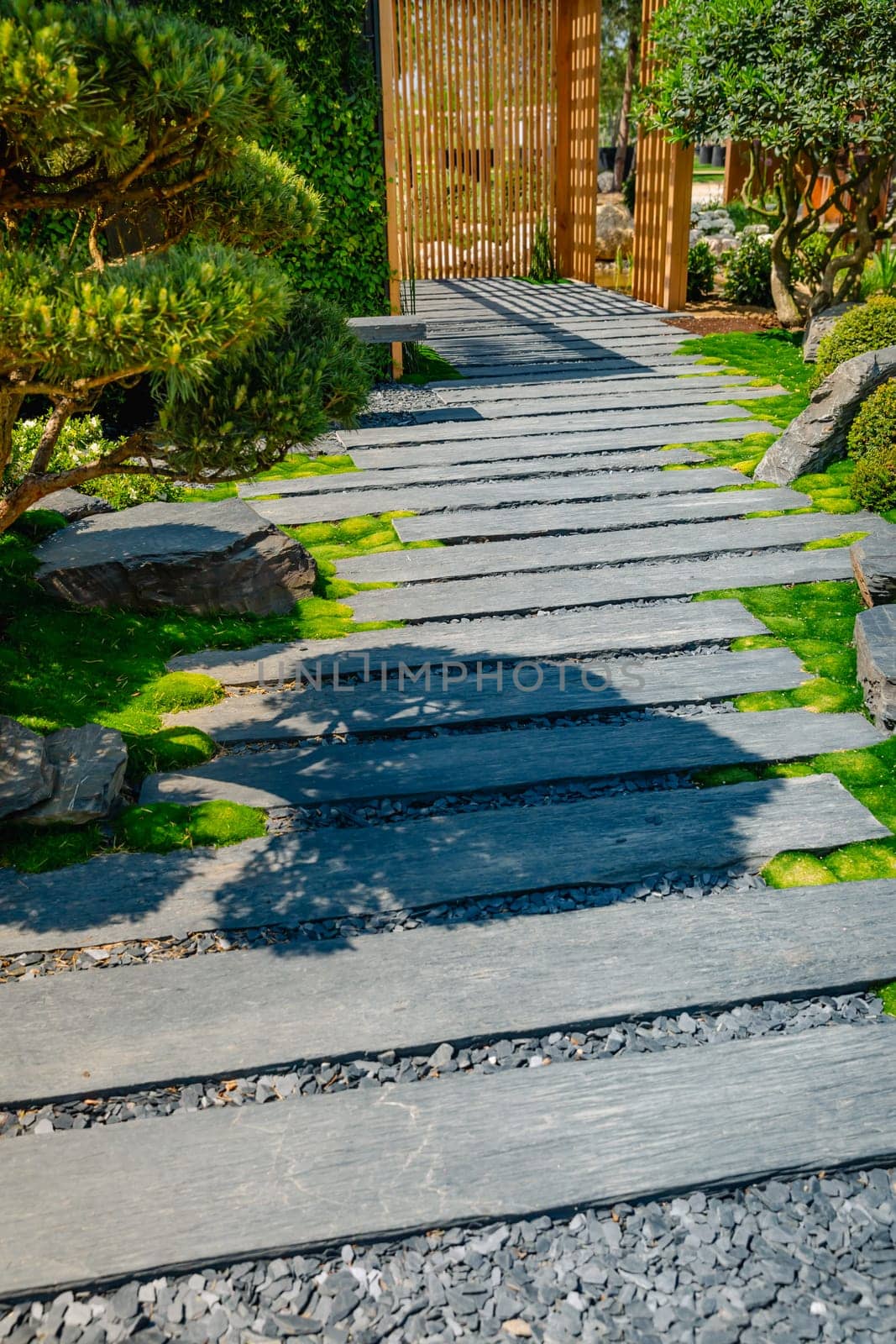 Detail of slate path with bark mulch and native plants in Japanese garden with wooden patio. Landscaping and gardening concept.