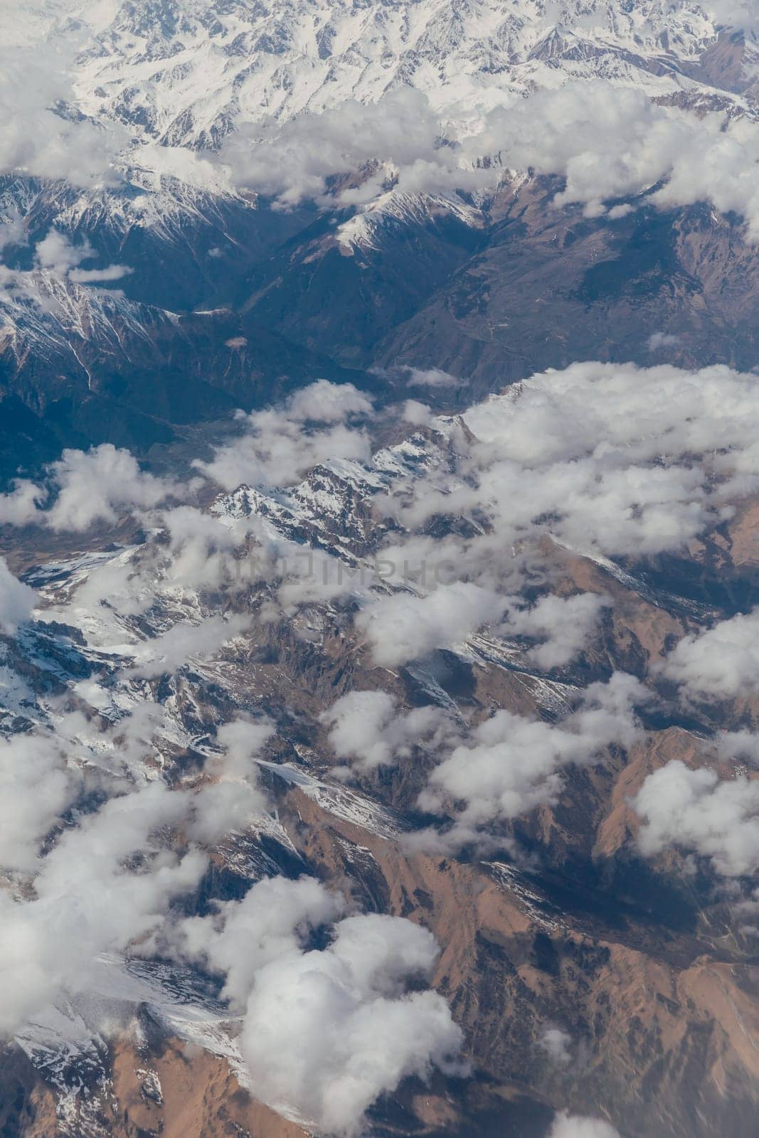 landscape on snowy mountains with clouds from the window of an airplane
