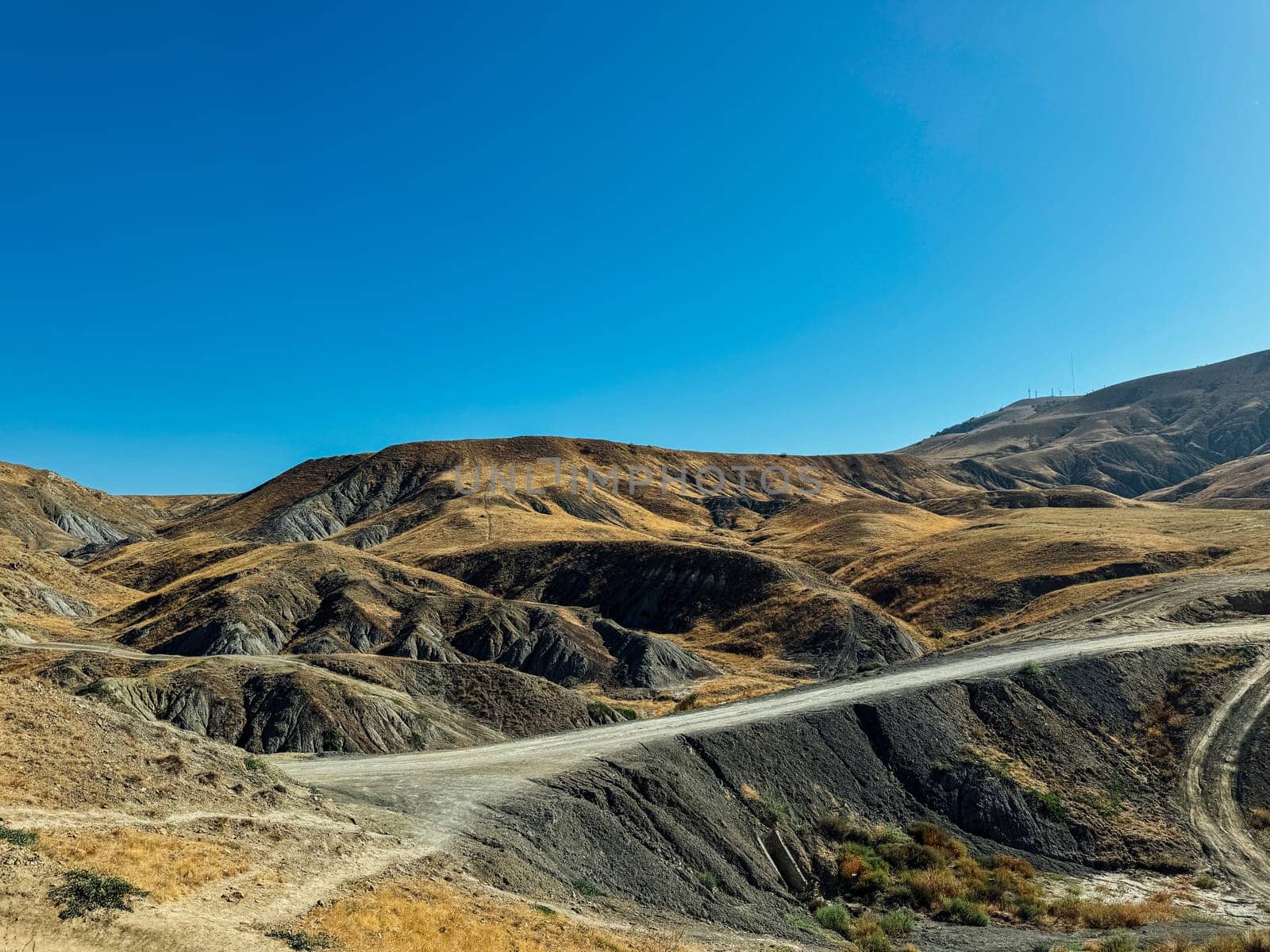 The road against the background of hills with dry grass and blue sky