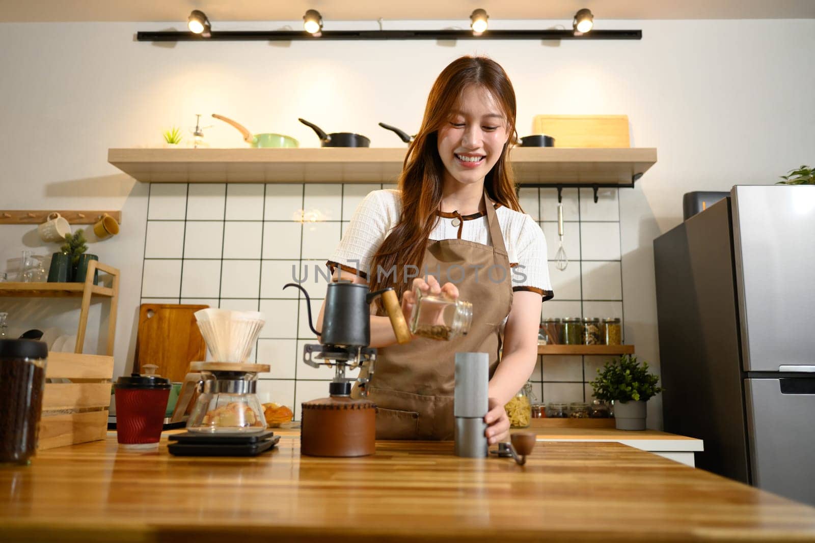 Happy woman in apron preparing pour over coffee at a wooden countertop.