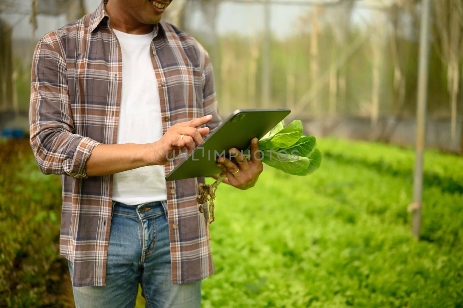 Smiling meal farmer using technology to assess crop quality inside a greenhouse. Smart farming concept.