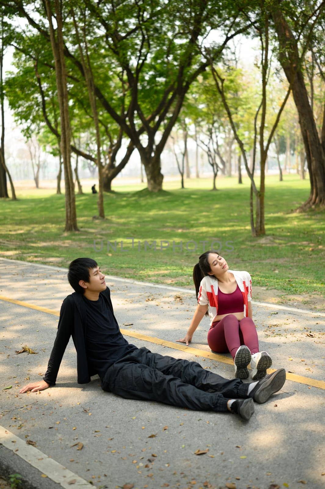 Tired man and woman sitting on a park pathway resting after a workout.