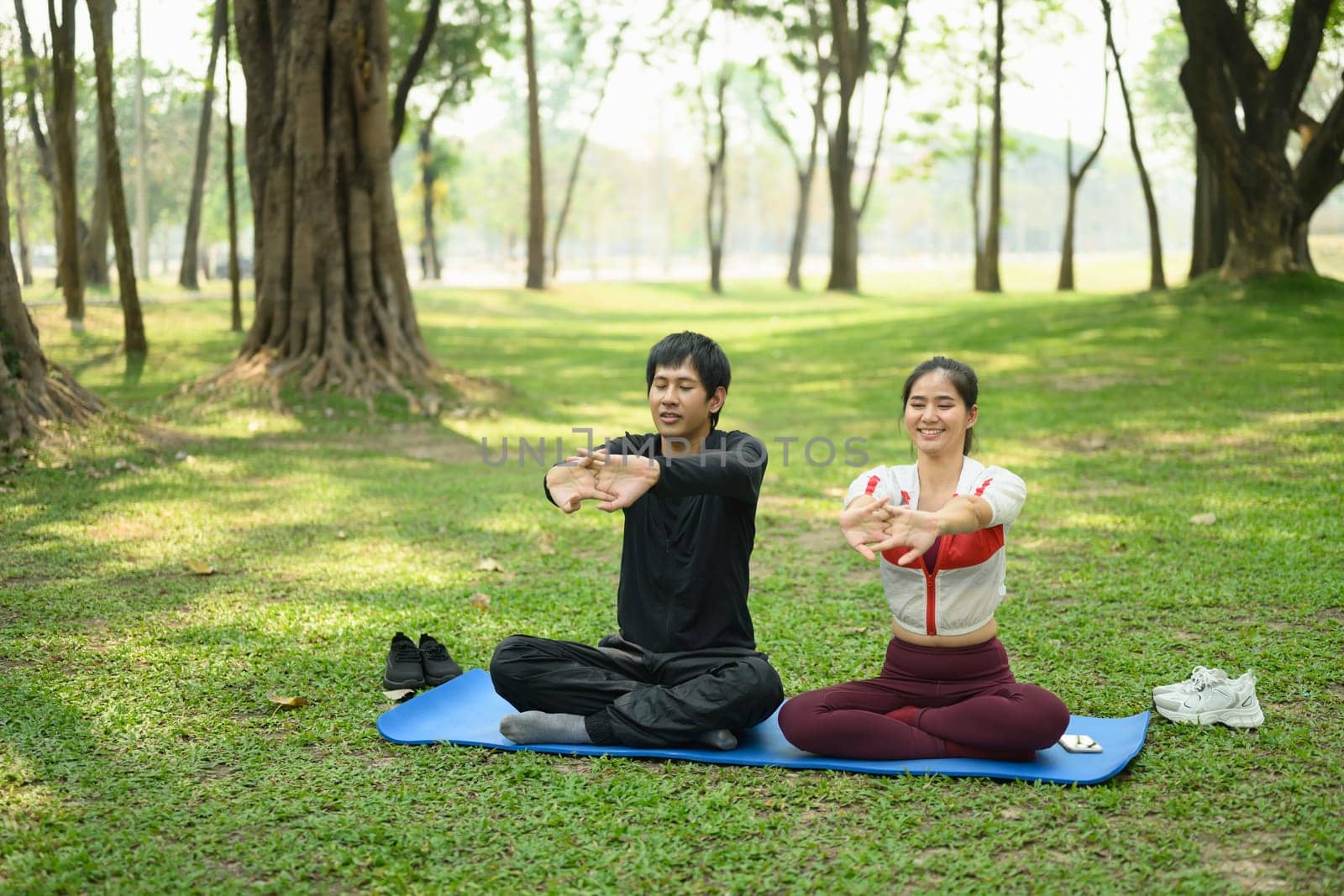 Young couple stretching on yoga mats in a peaceful park. Healthy lifestyle concept..