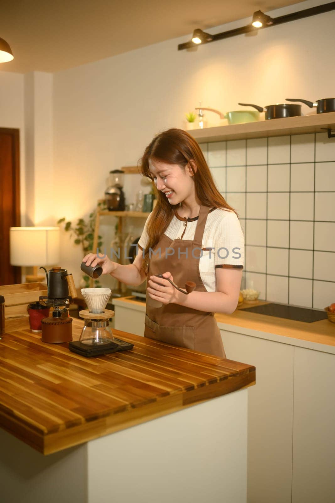 Happy woman in apron preparing pour over coffee at a wooden countertop.
