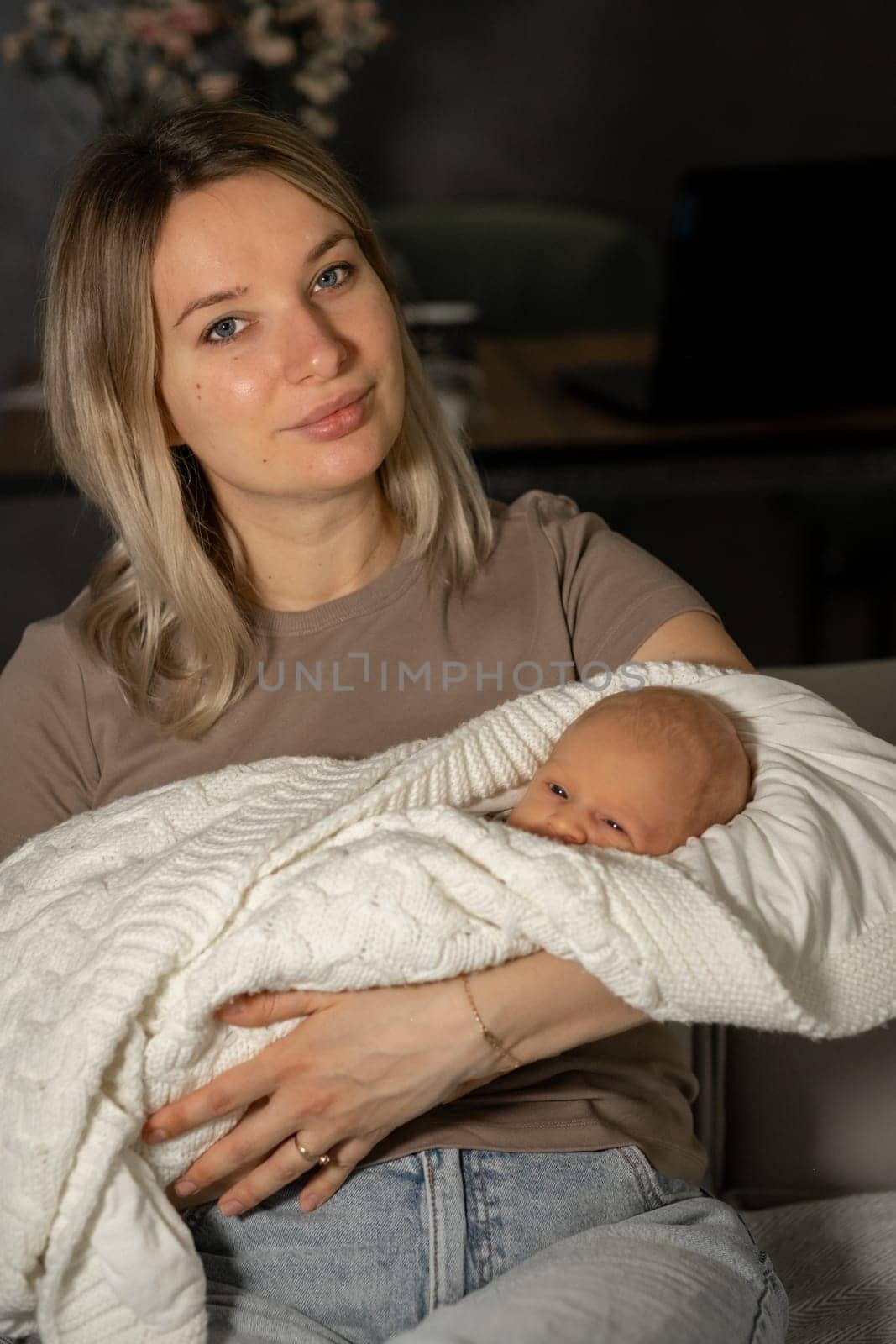 A mother cradles her baby in a soft blanket while sitting comfortably in a modern living room. The atmosphere is peaceful and serene, reflecting a close bond.