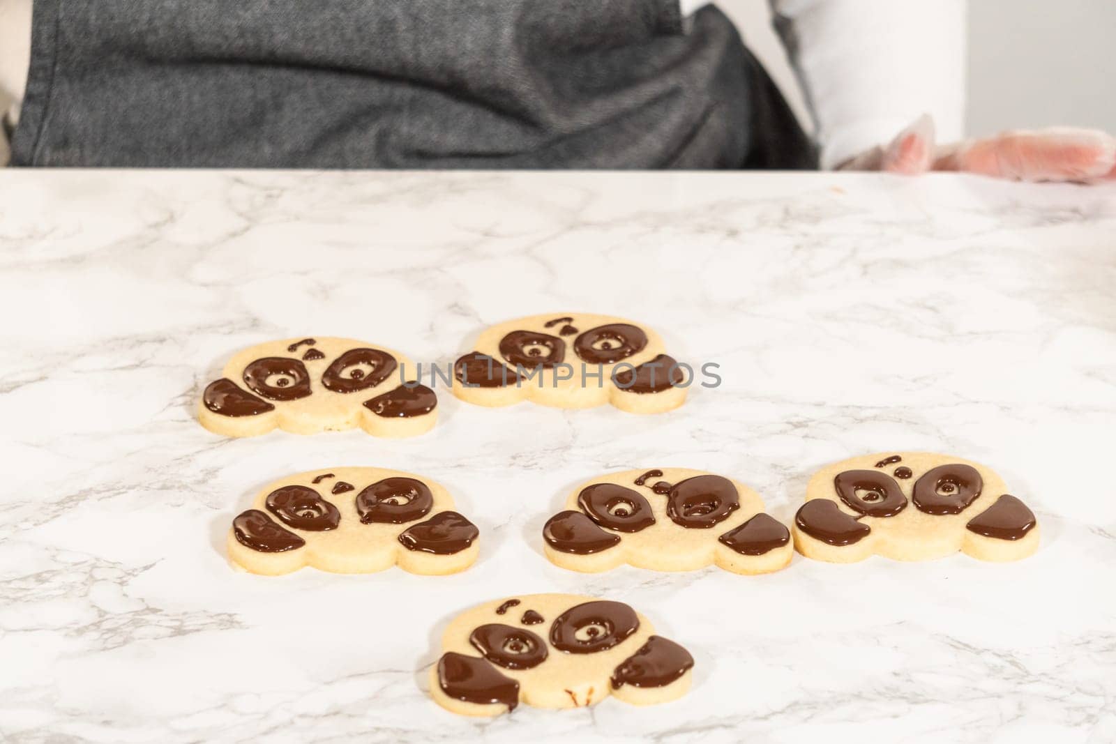 Full Batch of Panda Face Cookies Description: Front view of a full batch of decorated panda face cookies arranged on a marble surface, each detailed with chocolate royal icing for eyes, ears, and nose.