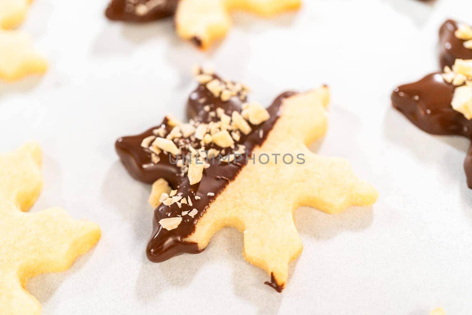 Creating cutout sugar cookies, partially dipped in chocolate and topped with hazelnut pieces, placed on parchment paper.