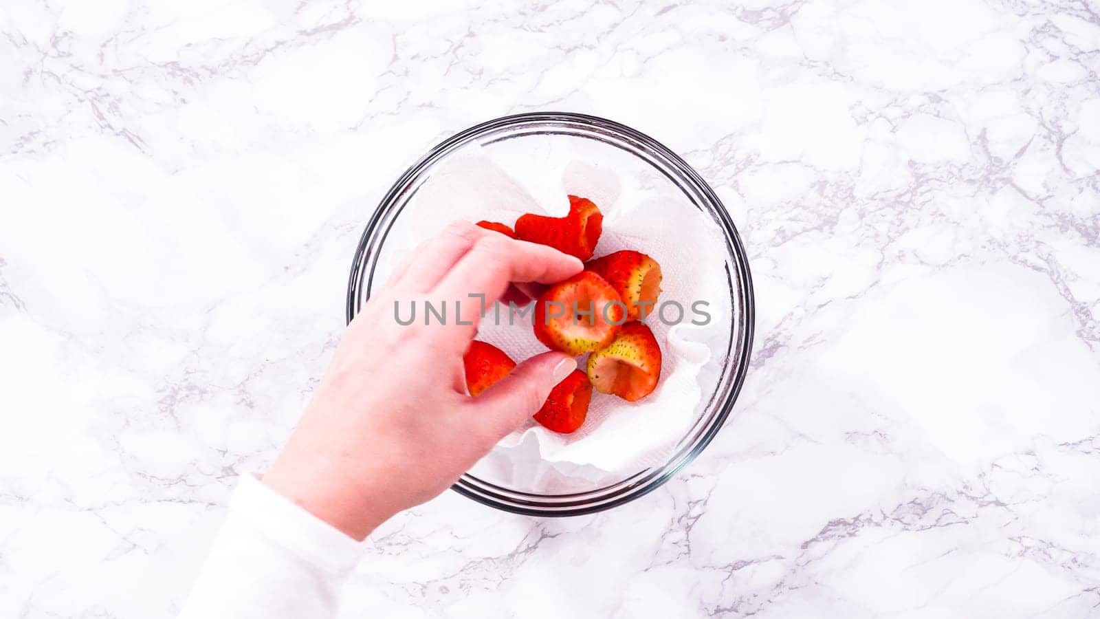 Flat lay. Strawberries, freshly washed and dried, are neatly stored in a glass bowl lined with a paper towel and securely covered with plastic wrap to maintain freshness.