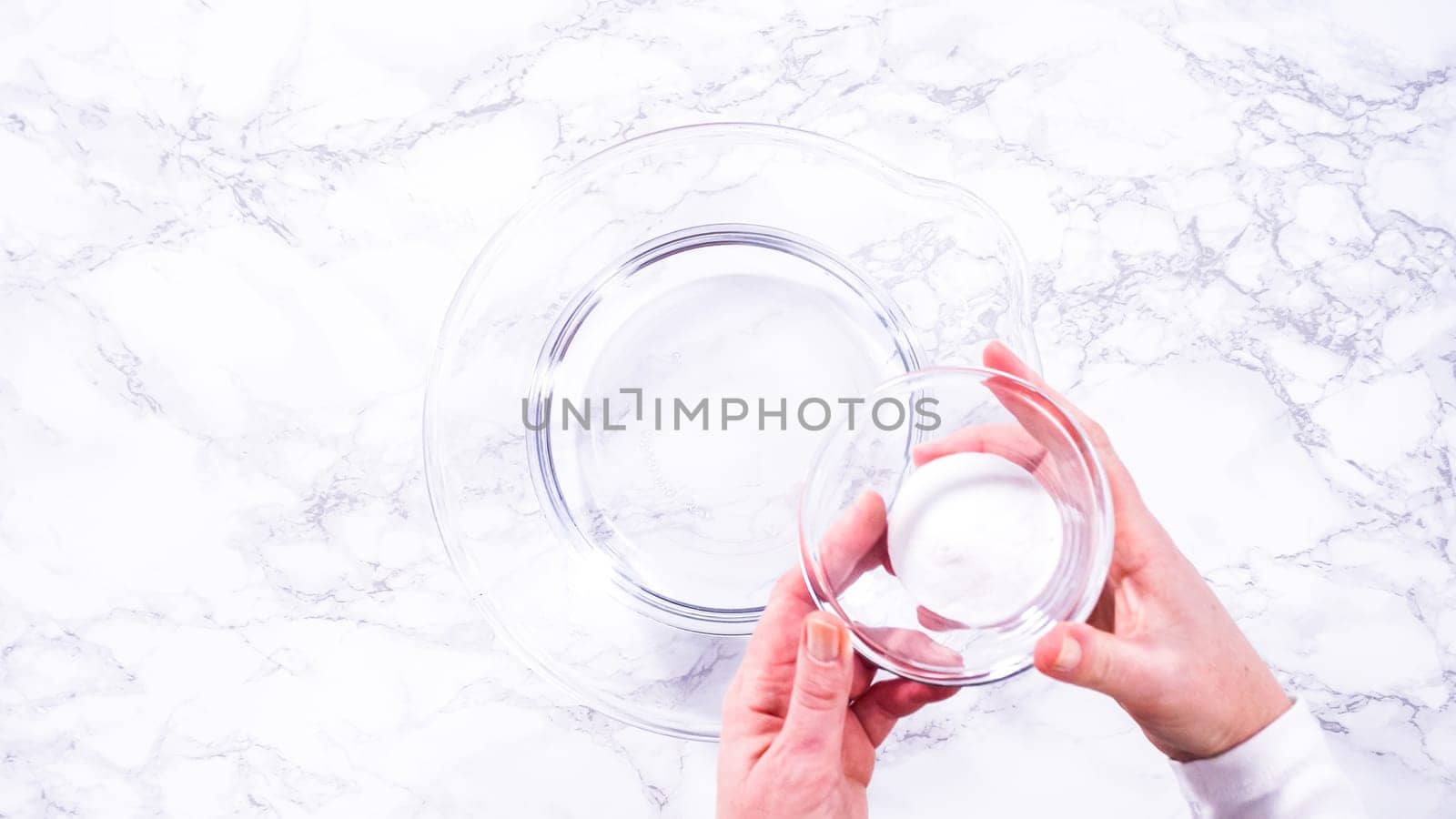 Flat lay. A spacious glass mixing bowl filled with water sits prepared to gently cleanse a batch of ripe strawberries, ensuring they are pristine before drying or storage.