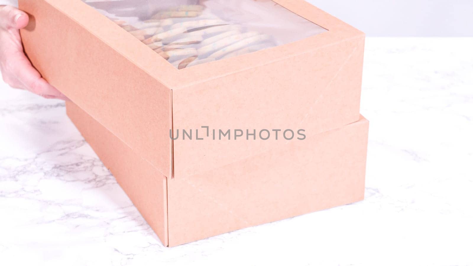 The sugar cookies, filled with sprinkles mixed into the dough, are carefully arranged with meticulous precision into a rustic brown paper box.
