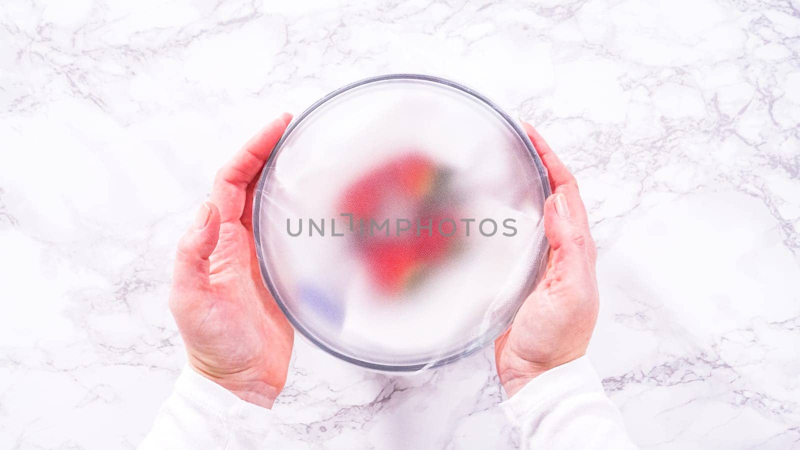 Flat lay. Strawberries, freshly washed and dried, are neatly stored in a glass bowl lined with a paper towel and securely covered with plastic wrap to maintain freshness.