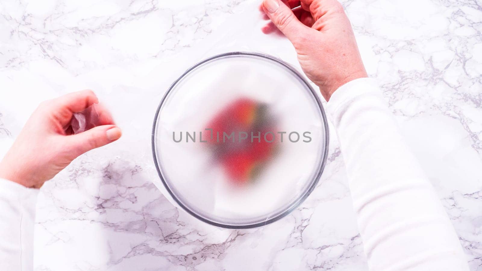 Flat lay. Strawberries, freshly washed and dried, are neatly stored in a glass bowl lined with a paper towel and securely covered with plastic wrap to maintain freshness.