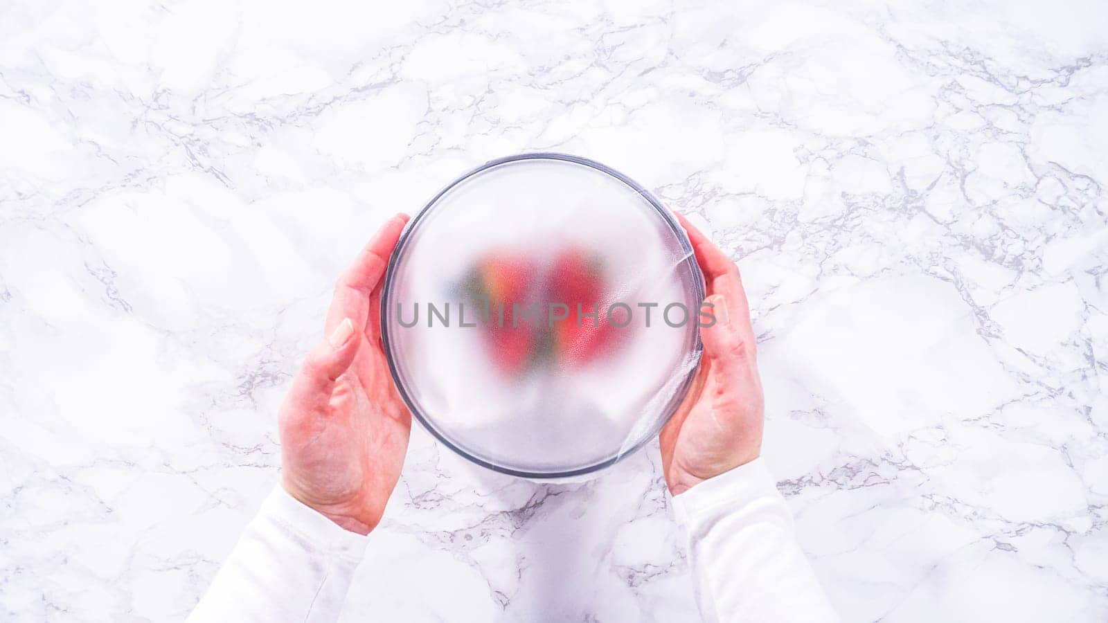 Flat lay. Strawberries, freshly washed and dried, are neatly stored in a glass bowl lined with a paper towel and securely covered with plastic wrap to maintain freshness.