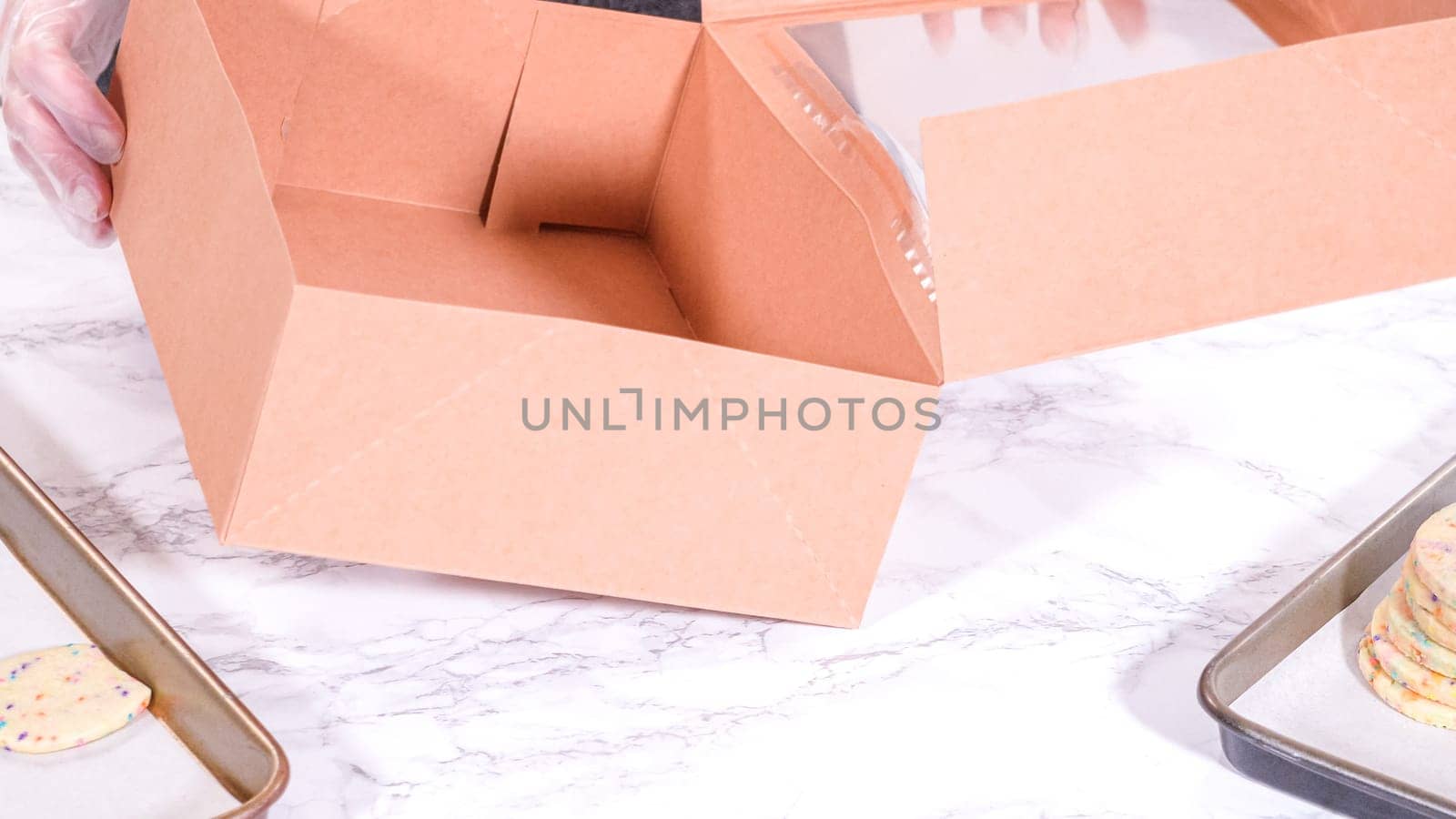 The sugar cookies, filled with sprinkles mixed into the dough, are carefully arranged with meticulous precision into a rustic brown paper box.