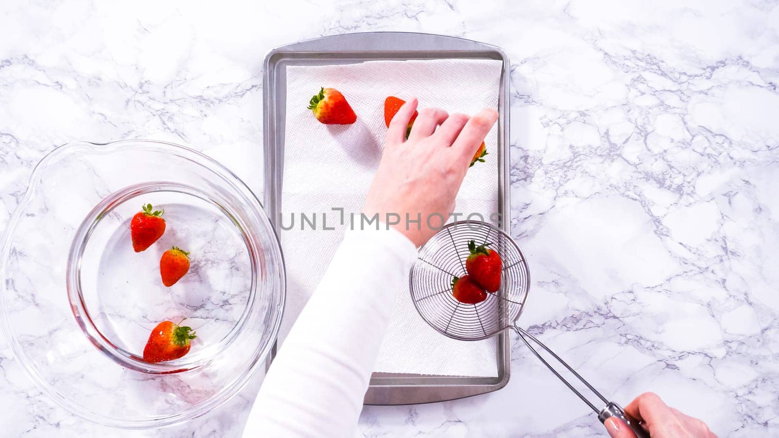 Flat lay. Juicy red strawberries, freshly washed, are spread out to dry on a baking sheet, carefully lined with paper towels to absorb excess moisture and prevent mold.