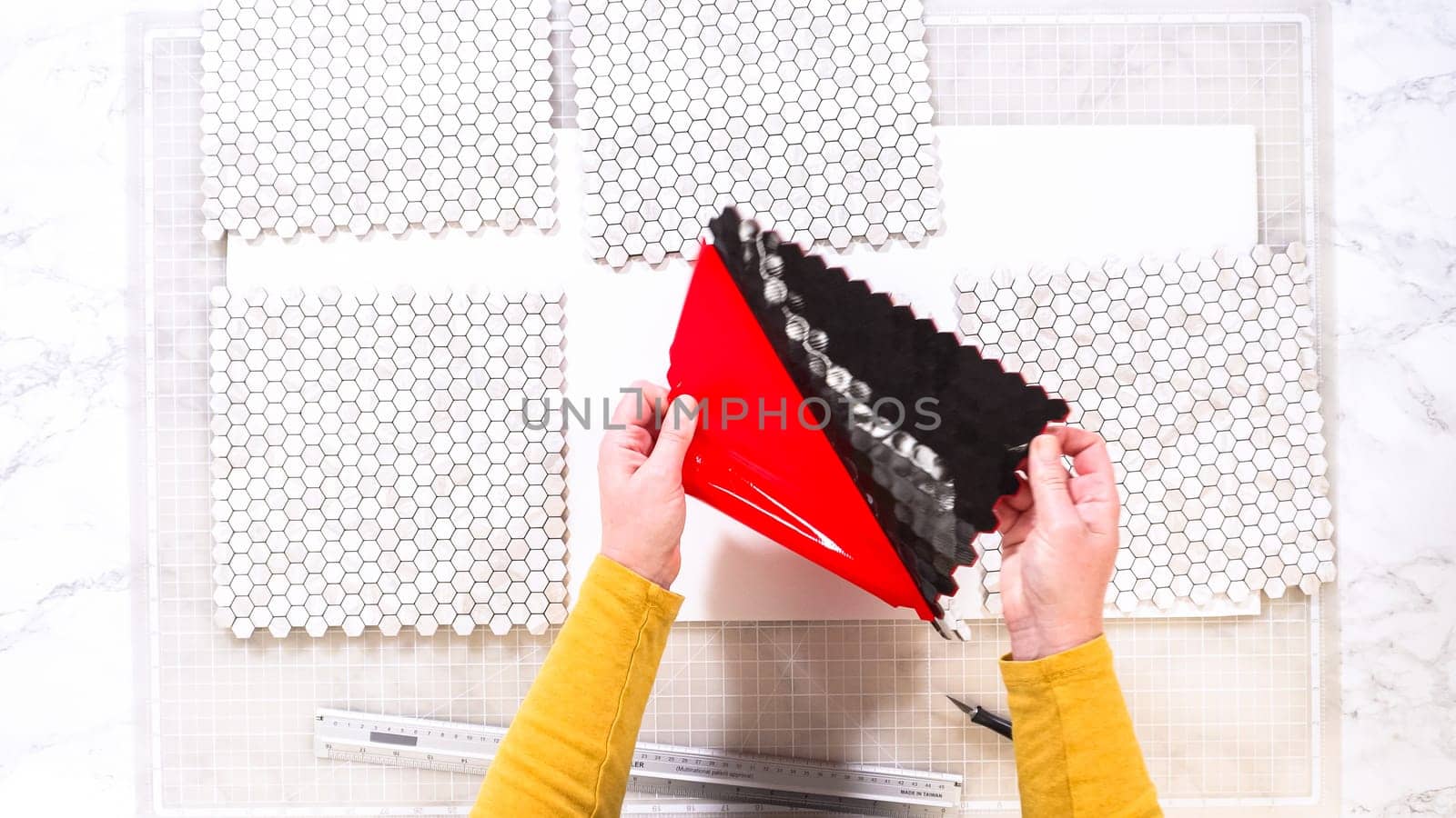 Flat lay. In the process of mounting peel and stick mosaic tiles onto a foam board, perfect for enhancing a food photography studio's aesthetic.