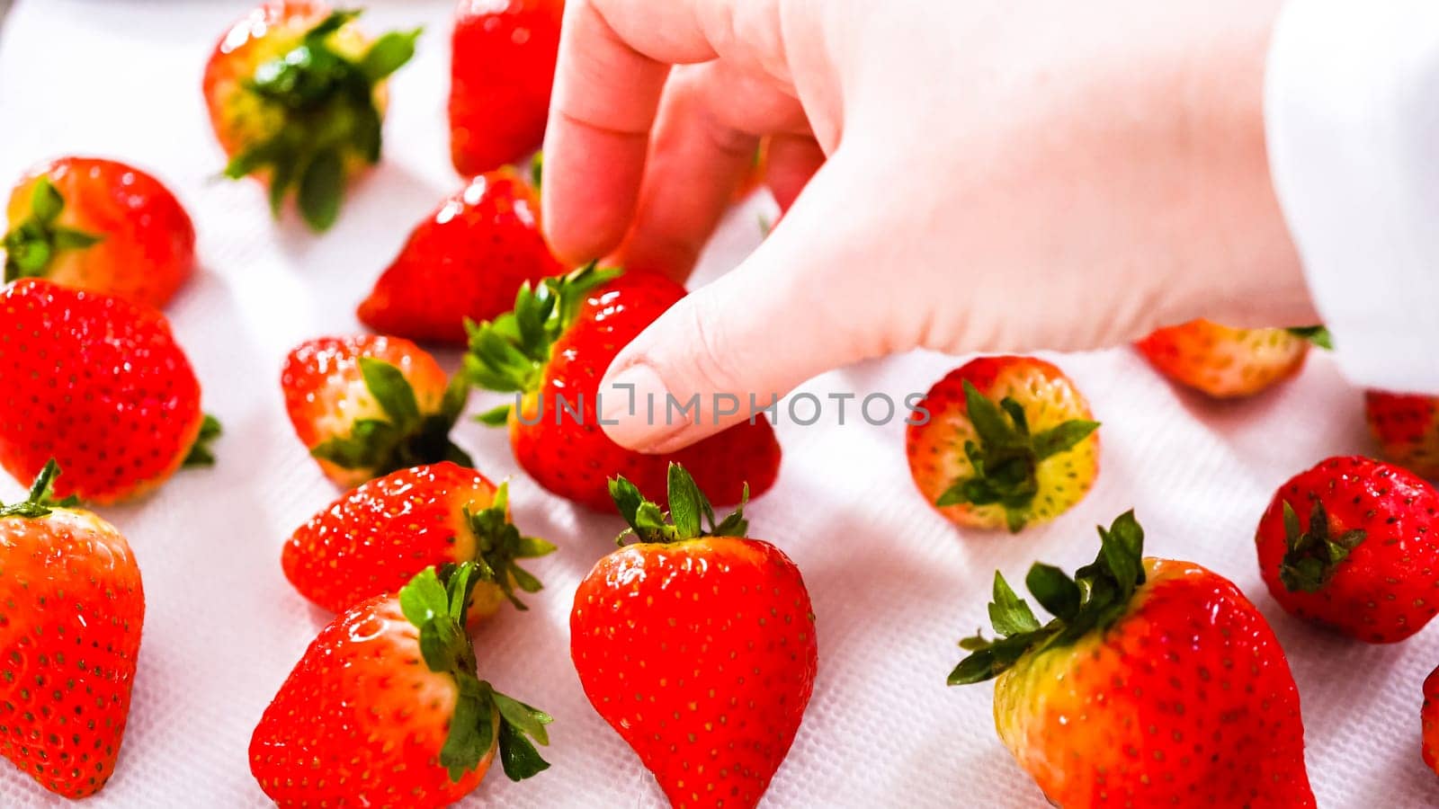 Juicy red strawberries, freshly washed, are spread out to dry on a baking sheet, carefully lined with paper towels to absorb excess moisture and prevent mold.