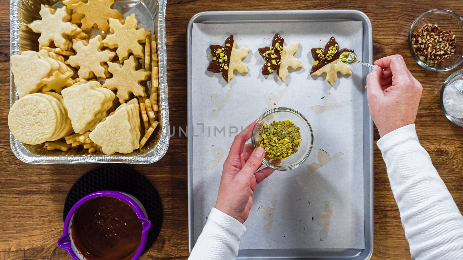 Flat lay. Creating snowflake-shaped cutout sugar cookies, dipped in chocolate, and adorned with different toppings.