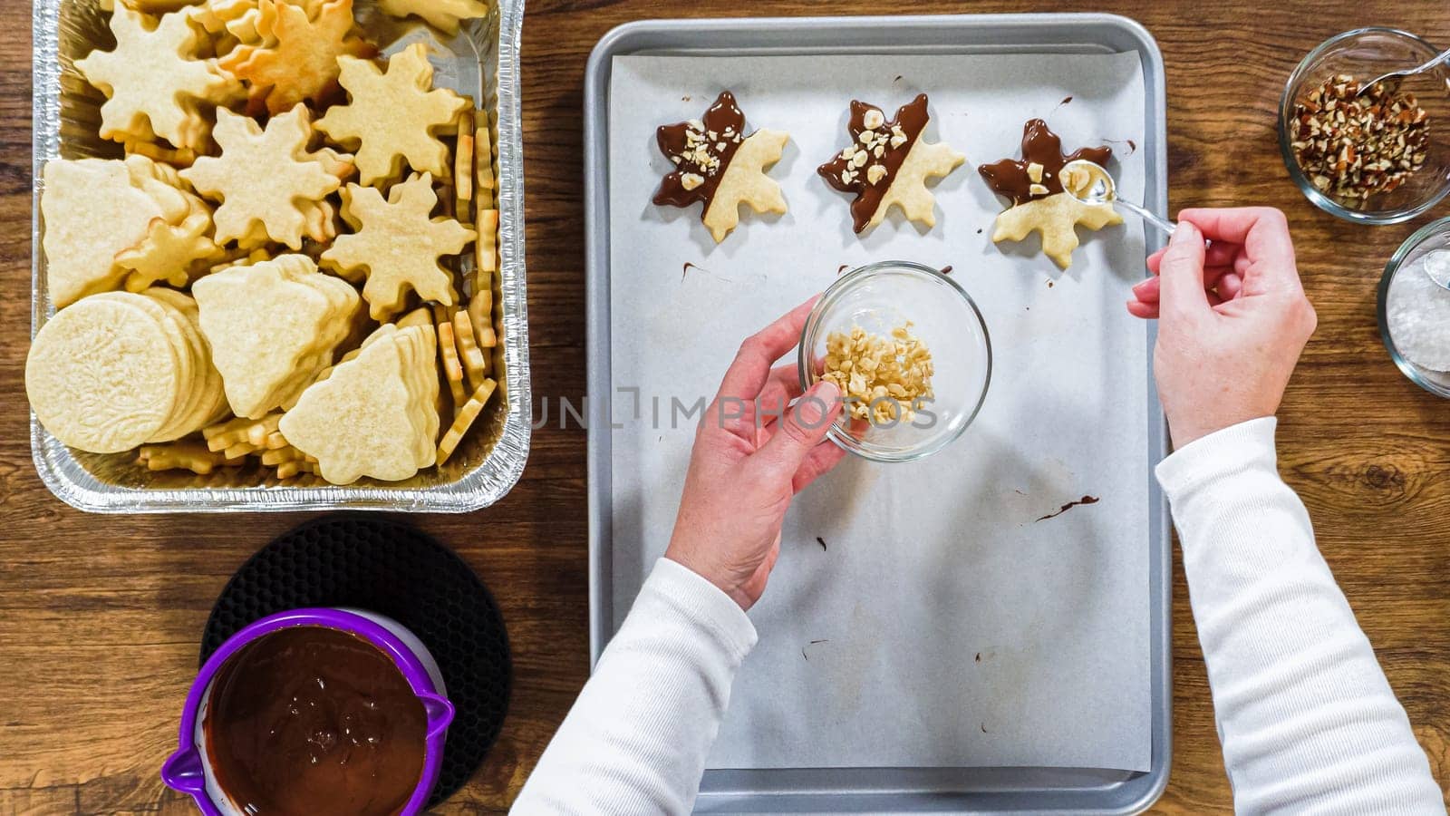 Flat lay. Creating snowflake-shaped cutout sugar cookies, dipped in chocolate, and adorned with different toppings.