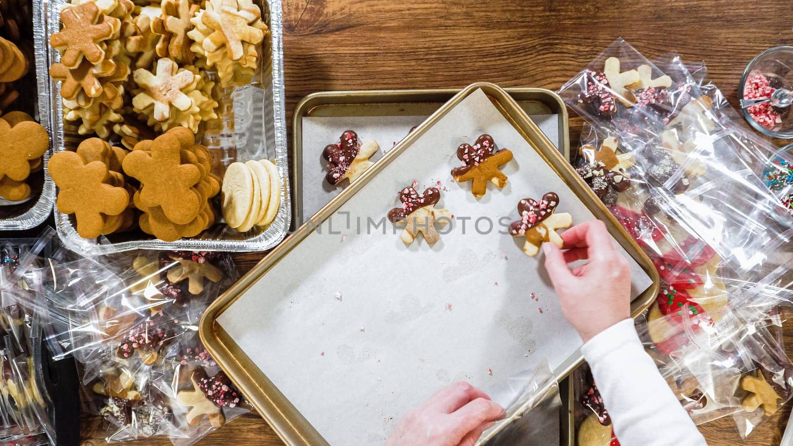Flat lay. Carefully packaging Christmas cutout cookies, half-dipped in chocolate, sprinkled with crushed nuts, and presented in clear cellophane wrapping.