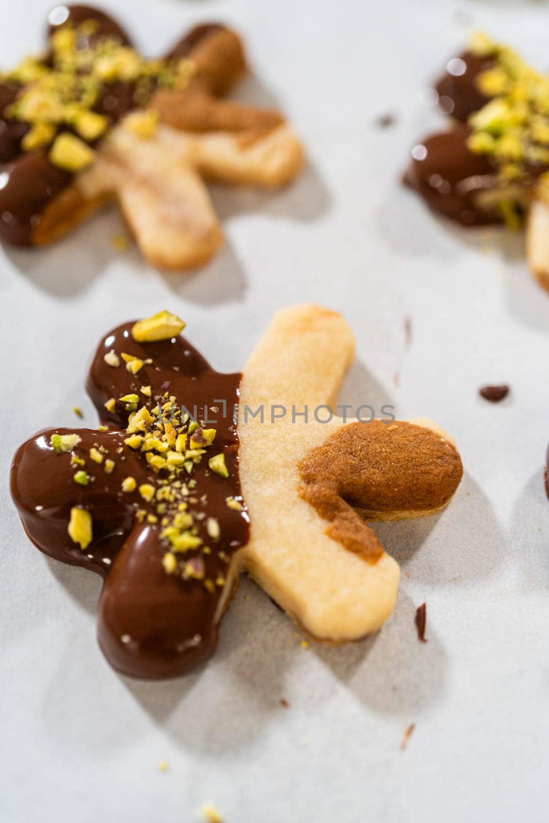 Crafting star-shaped holiday cookies dipped in chocolate and sprinkled with crushed pistachios, arranged on parchment paper.