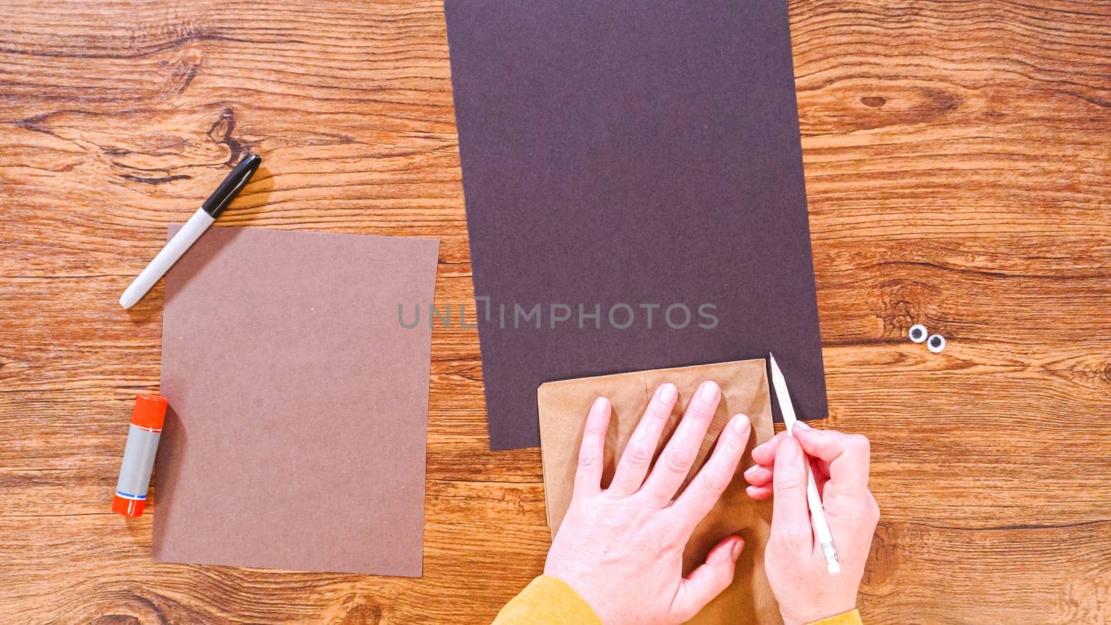 Step by step. Flat lay. Teacher guides online class through making a paper puppet from a brown bag, creatively using a wooden surface as a workspace.