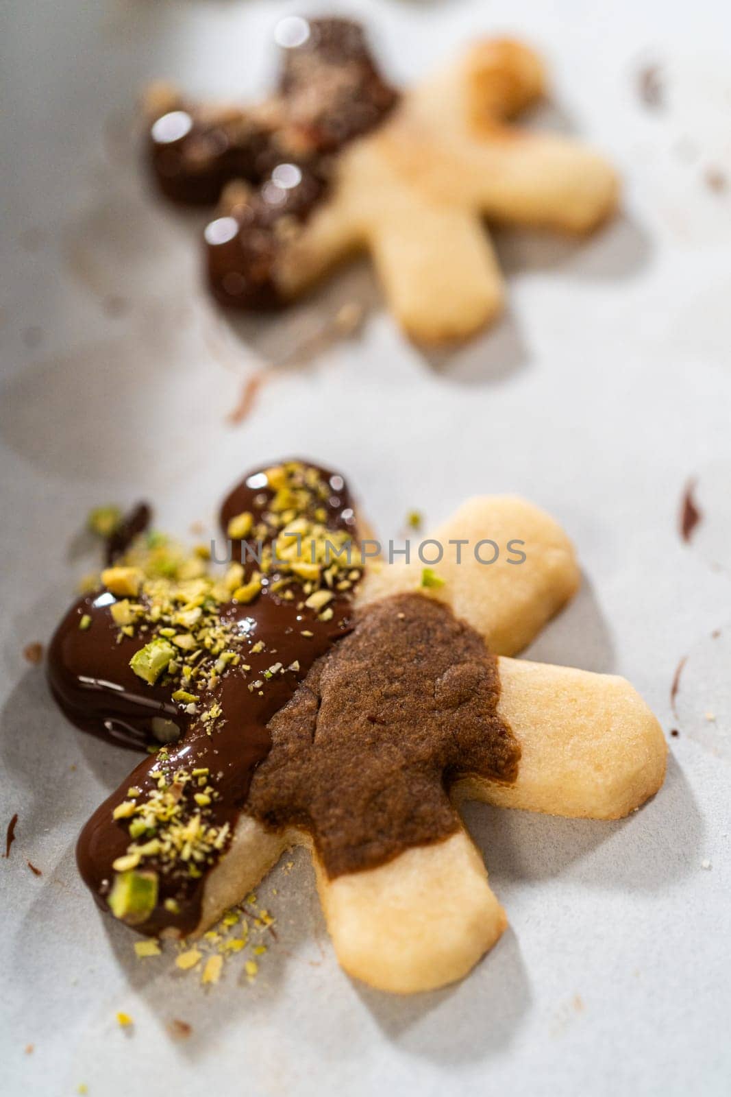 Crafting star-shaped holiday cookies dipped in chocolate and sprinkled with crushed pistachios, arranged on parchment paper.