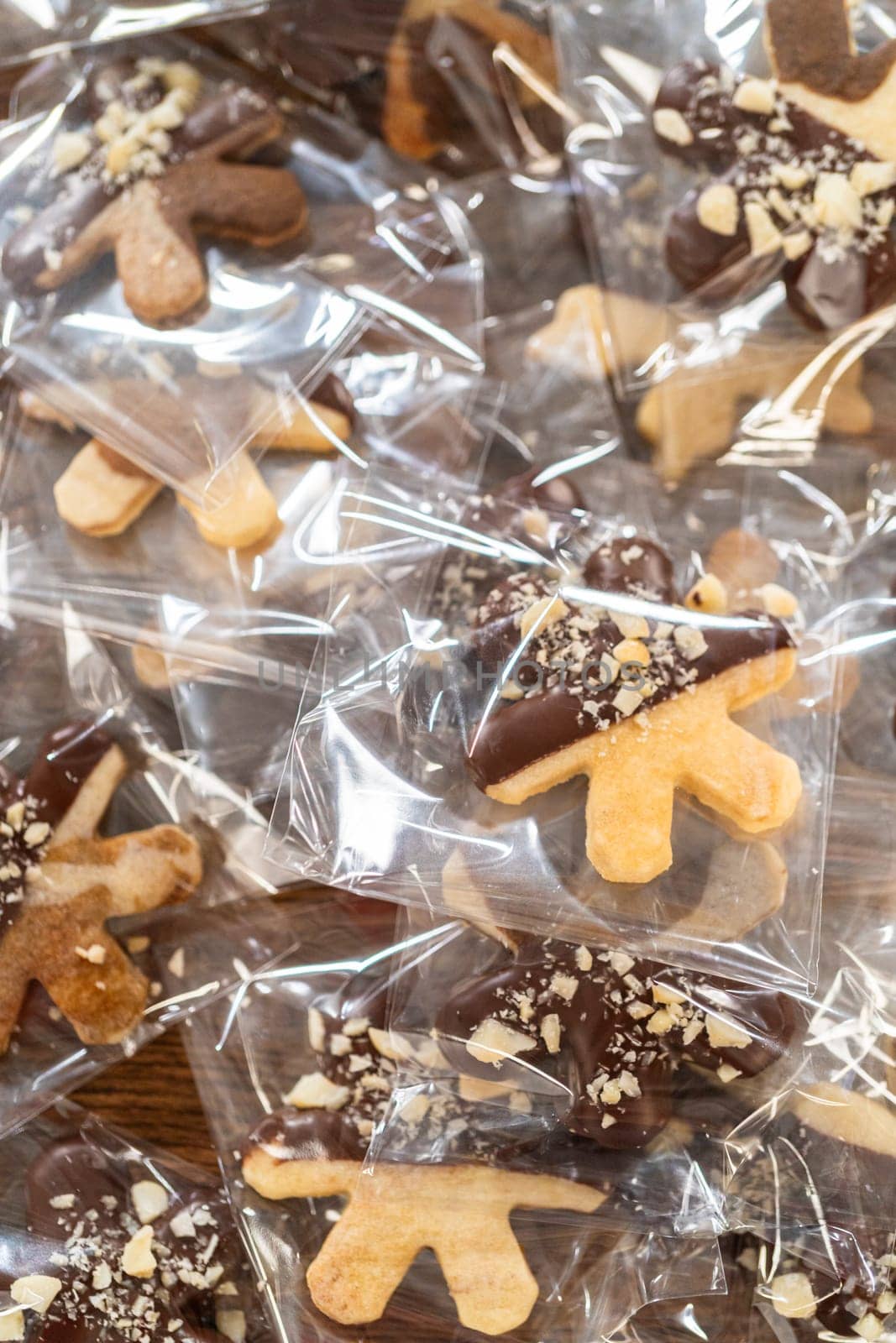 Carefully packaging Christmas cutout cookies, half-dipped in chocolate and presented in clear cellophane wrapping, perfect for festive gifting.