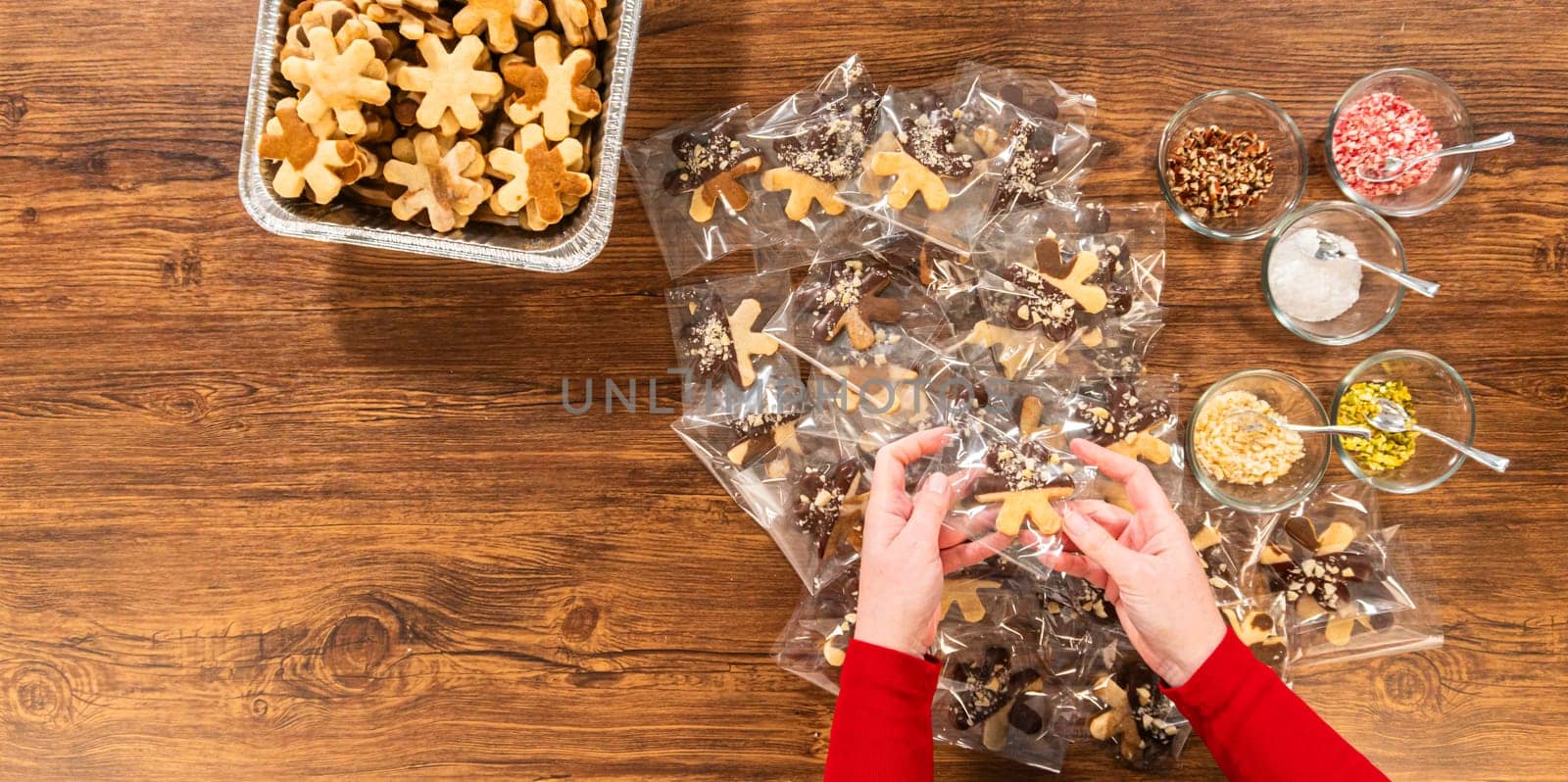 Carefully packaging Christmas cutout cookies, half-dipped in chocolate and presented in clear cellophane wrapping, perfect for festive gifting.