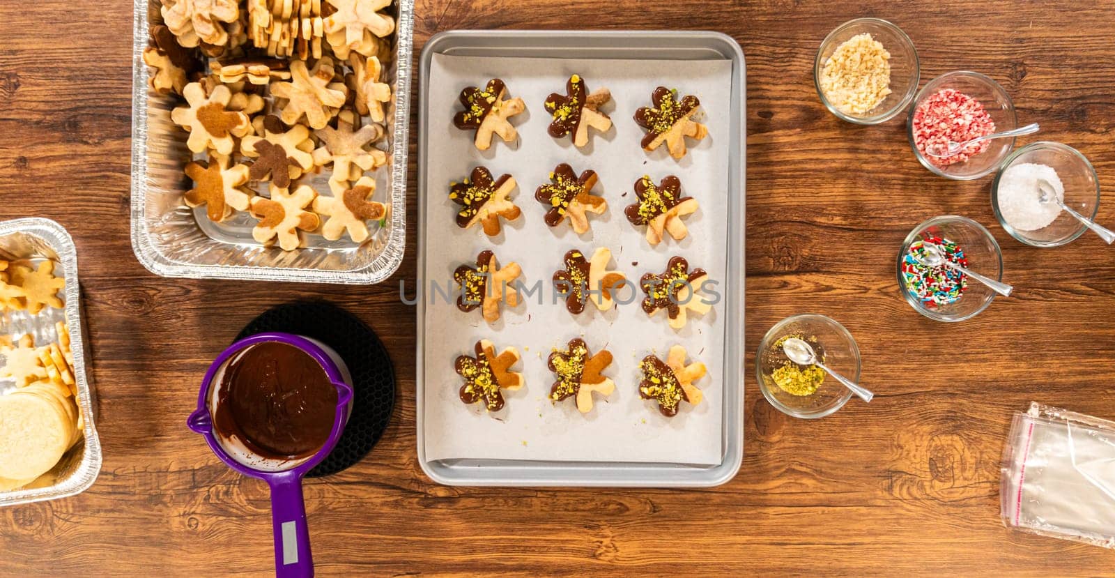 Crafting star-shaped holiday cookies dipped in chocolate and sprinkled with crushed pistachios, arranged on parchment paper.