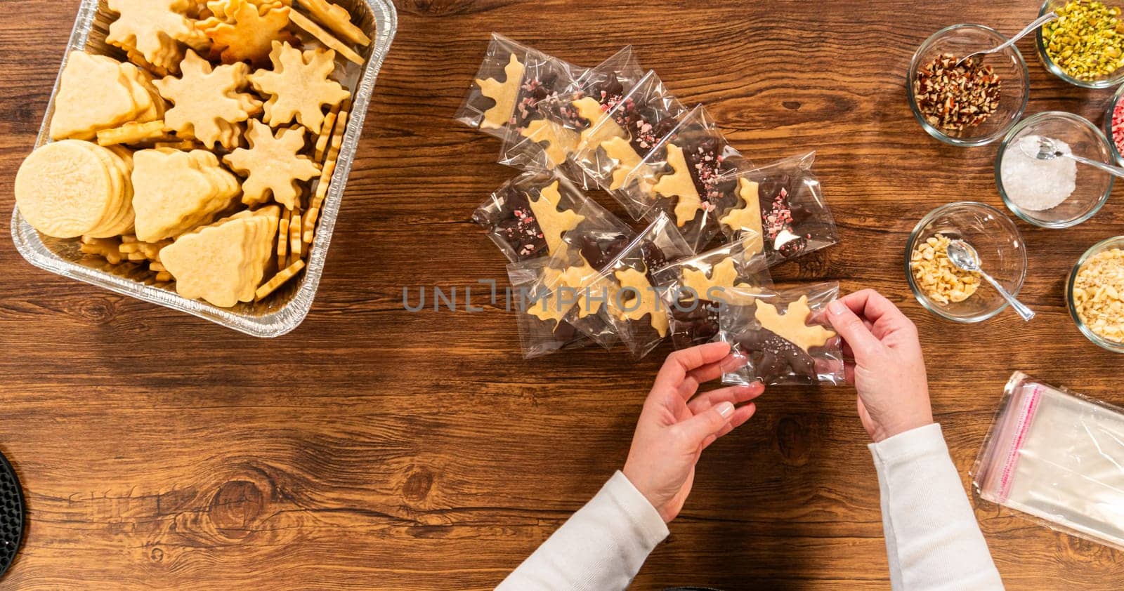 Carefully packaging Christmas cutout cookies, half-dipped in chocolate and presented in clear cellophane wrapping, perfect for festive gifting.