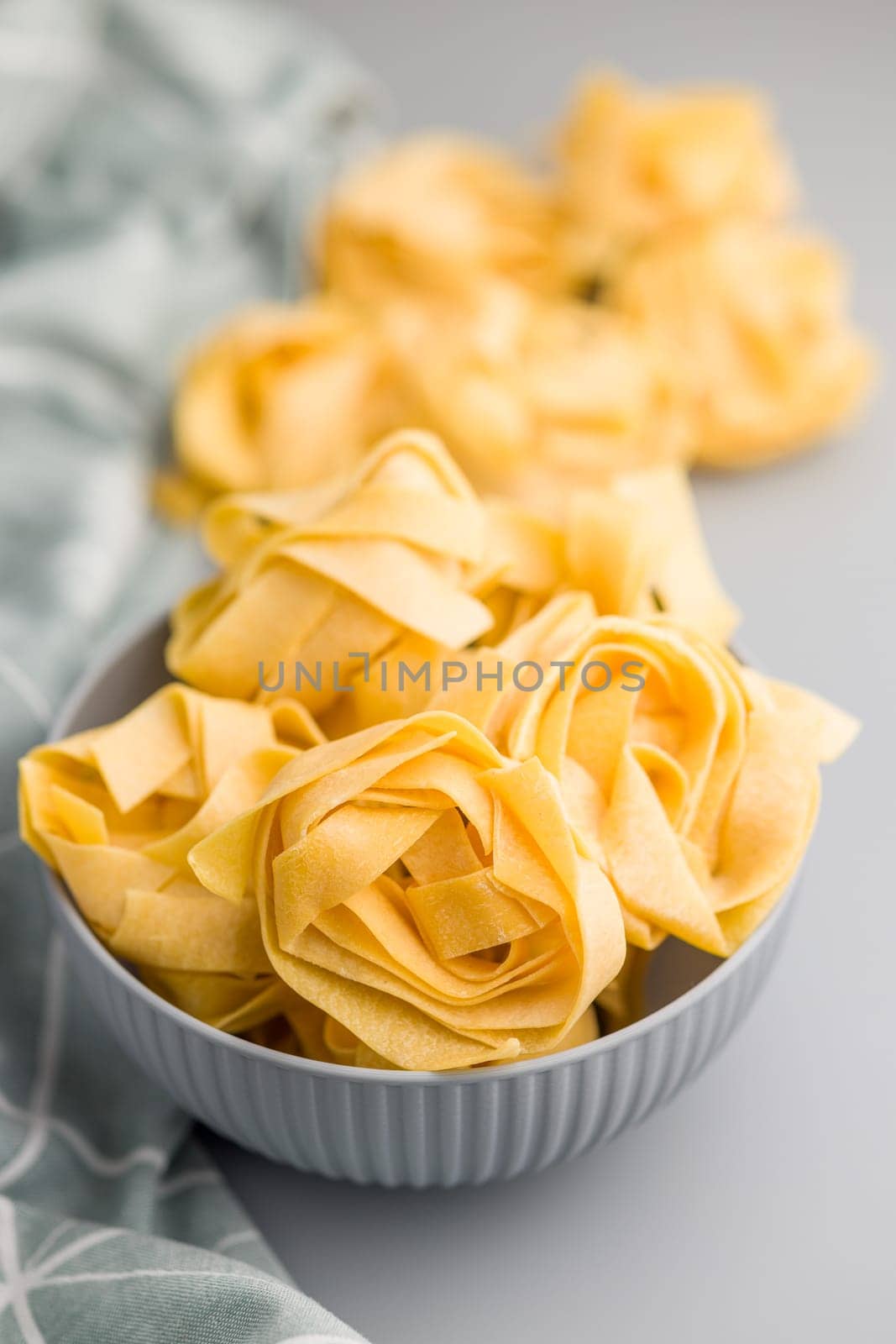 Italian pasta tagliatelle. Uncooked noodle pasta in bowl on a gray background.