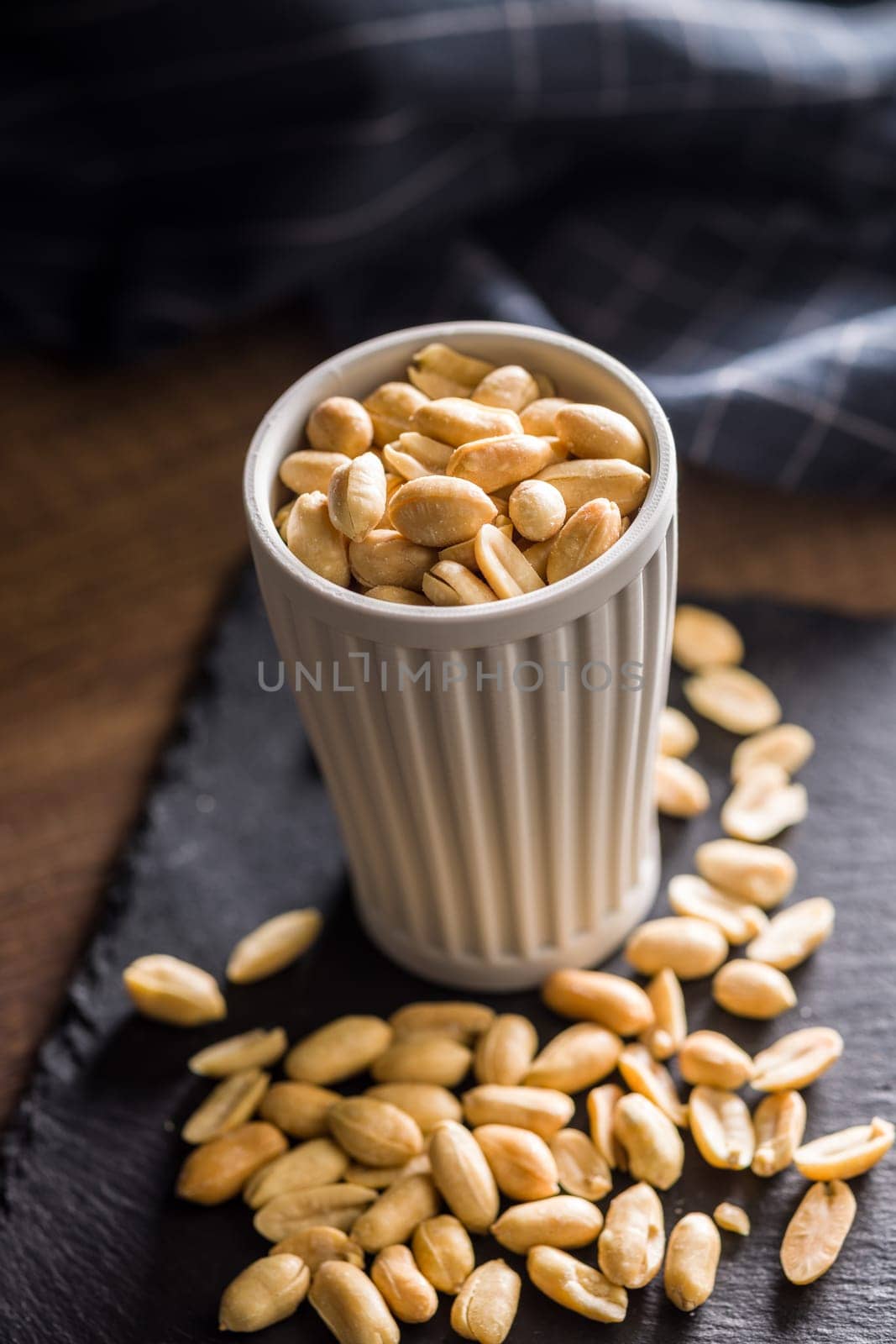 Roasted salted peanuts in cup on a wooden table.